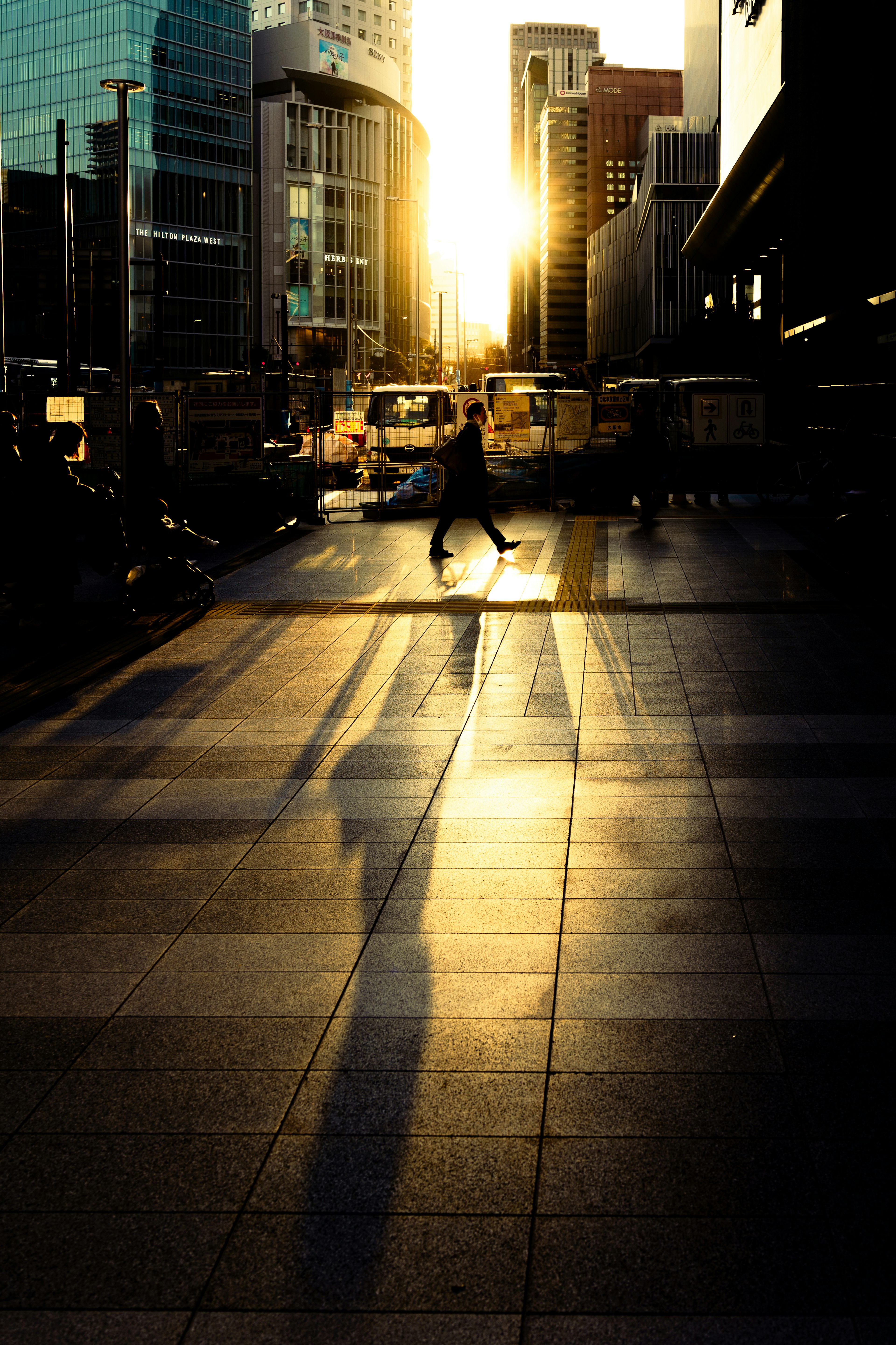 Silueta de una persona caminando por una calle de la ciudad con reflejos del atardecer