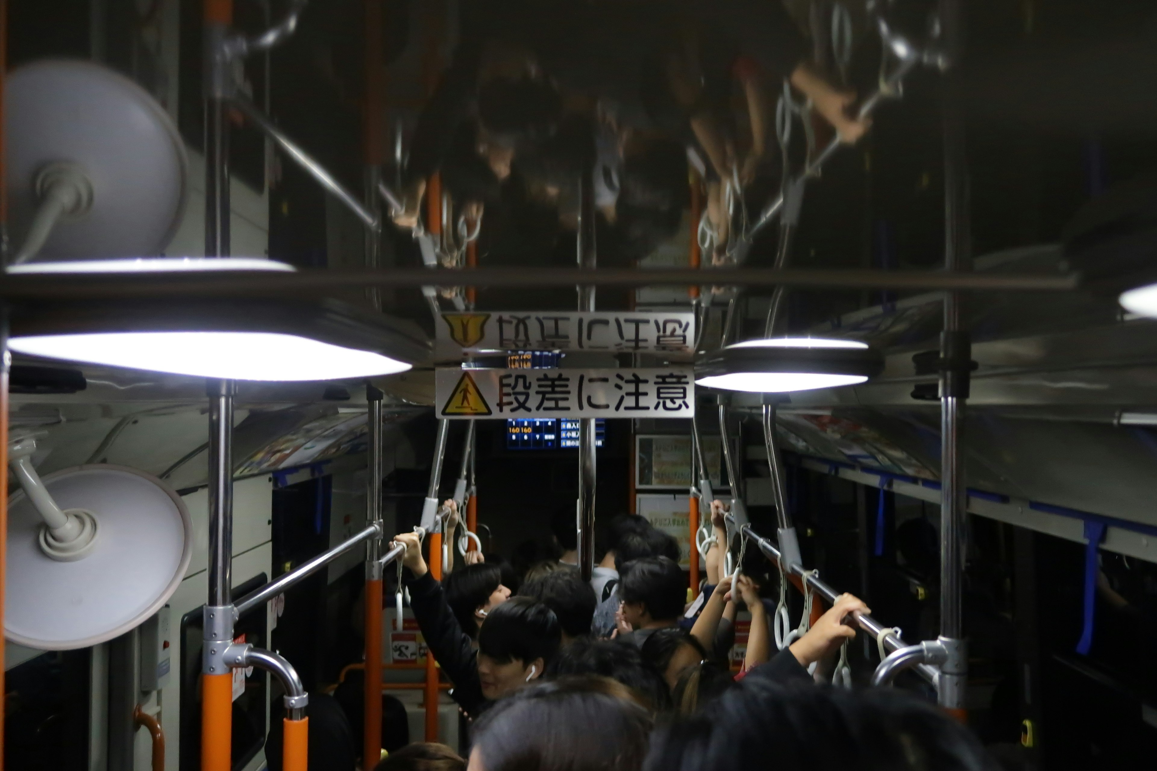 Intérieur d'un bus faiblement éclairé avec des passagers tenant des sangles et des réflexions au plafond