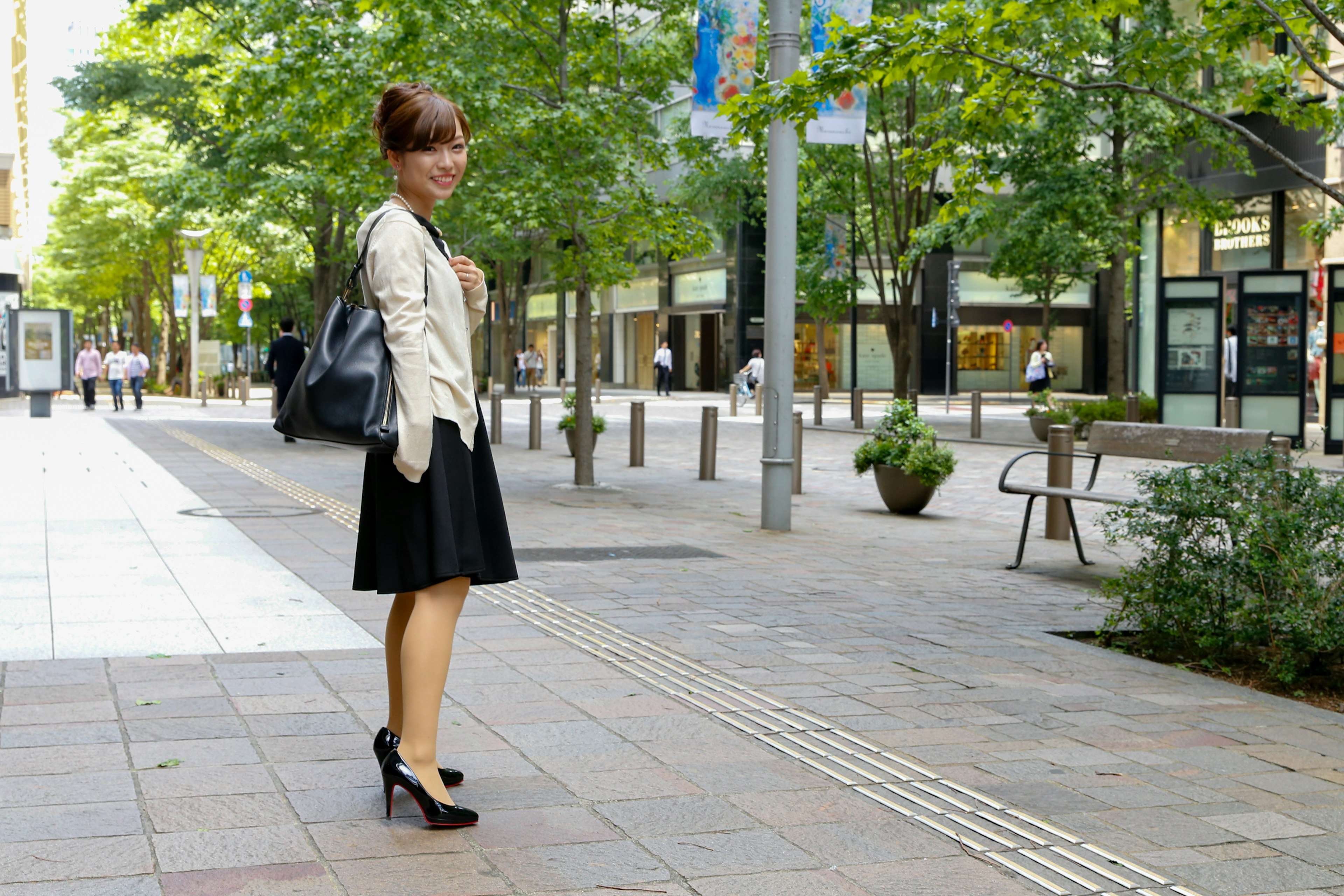 Woman in black skirt and jacket standing on a tree-lined street