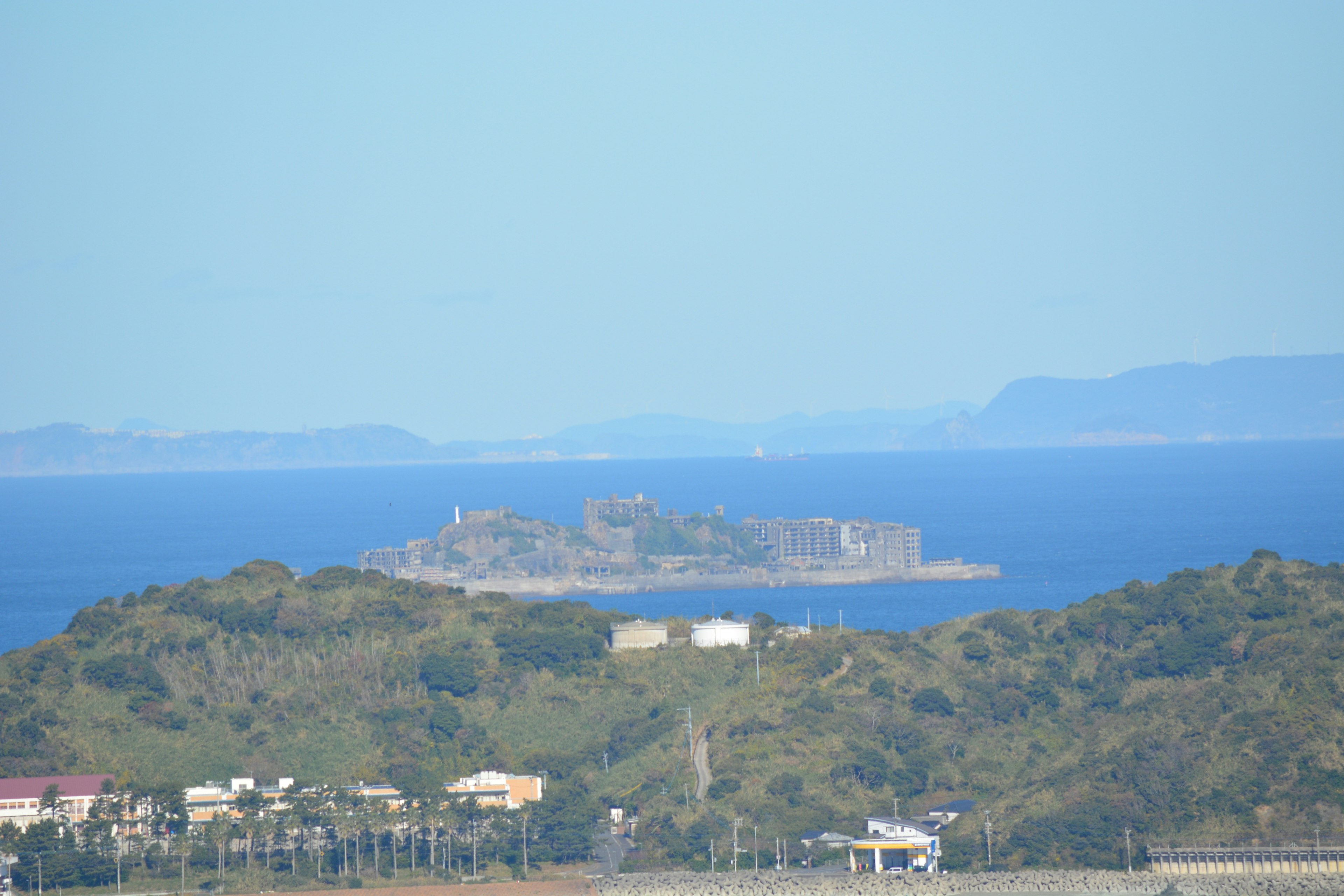 A small island with a fort in the distance surrounded by blue ocean and green hills