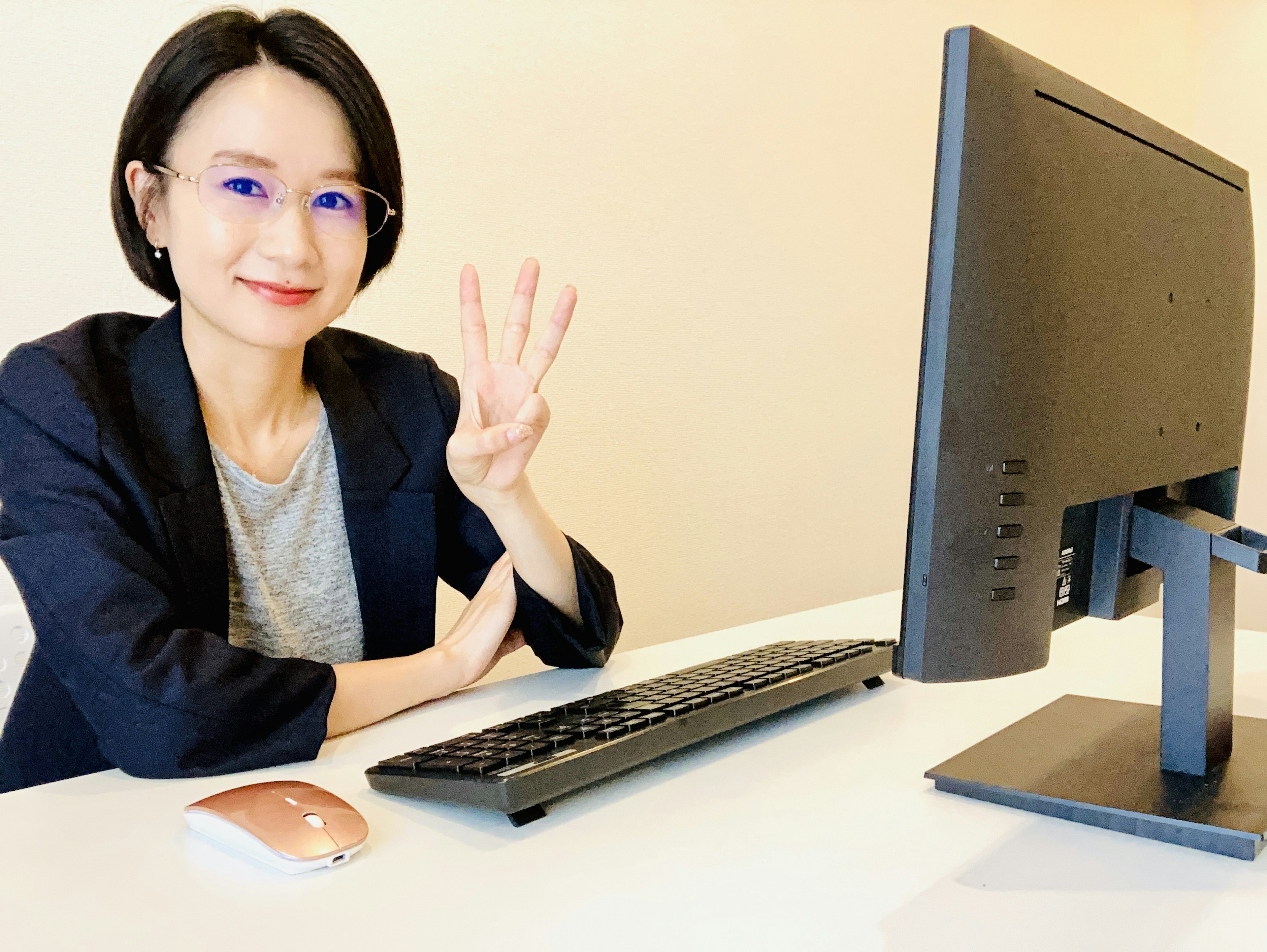 Eine Frau sitzt an einem Schreibtisch mit einem Computer und zeigt ein Friedenszeichen