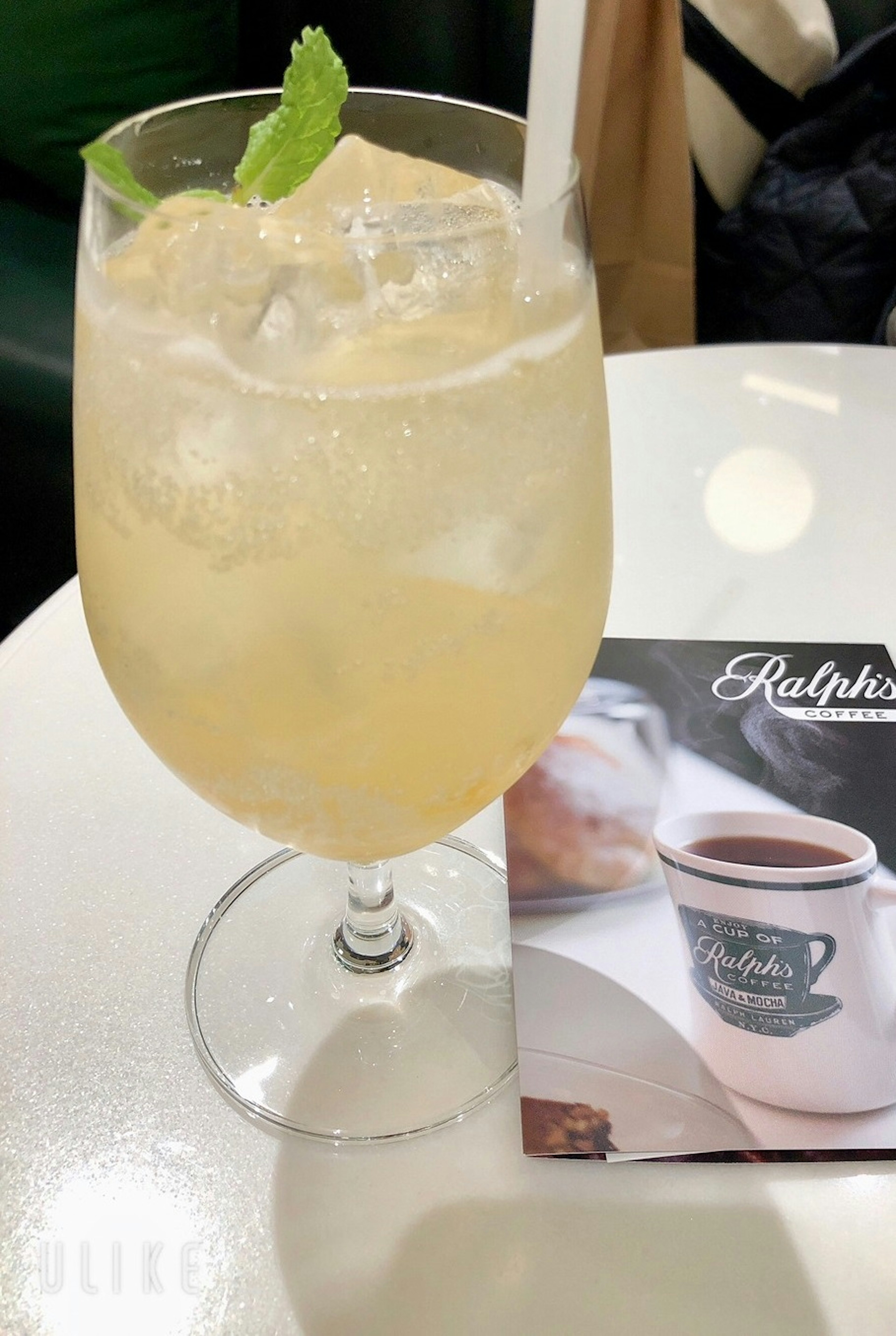 A refreshing drink in a clear glass with ice and a mint leaf beside a menu on a table