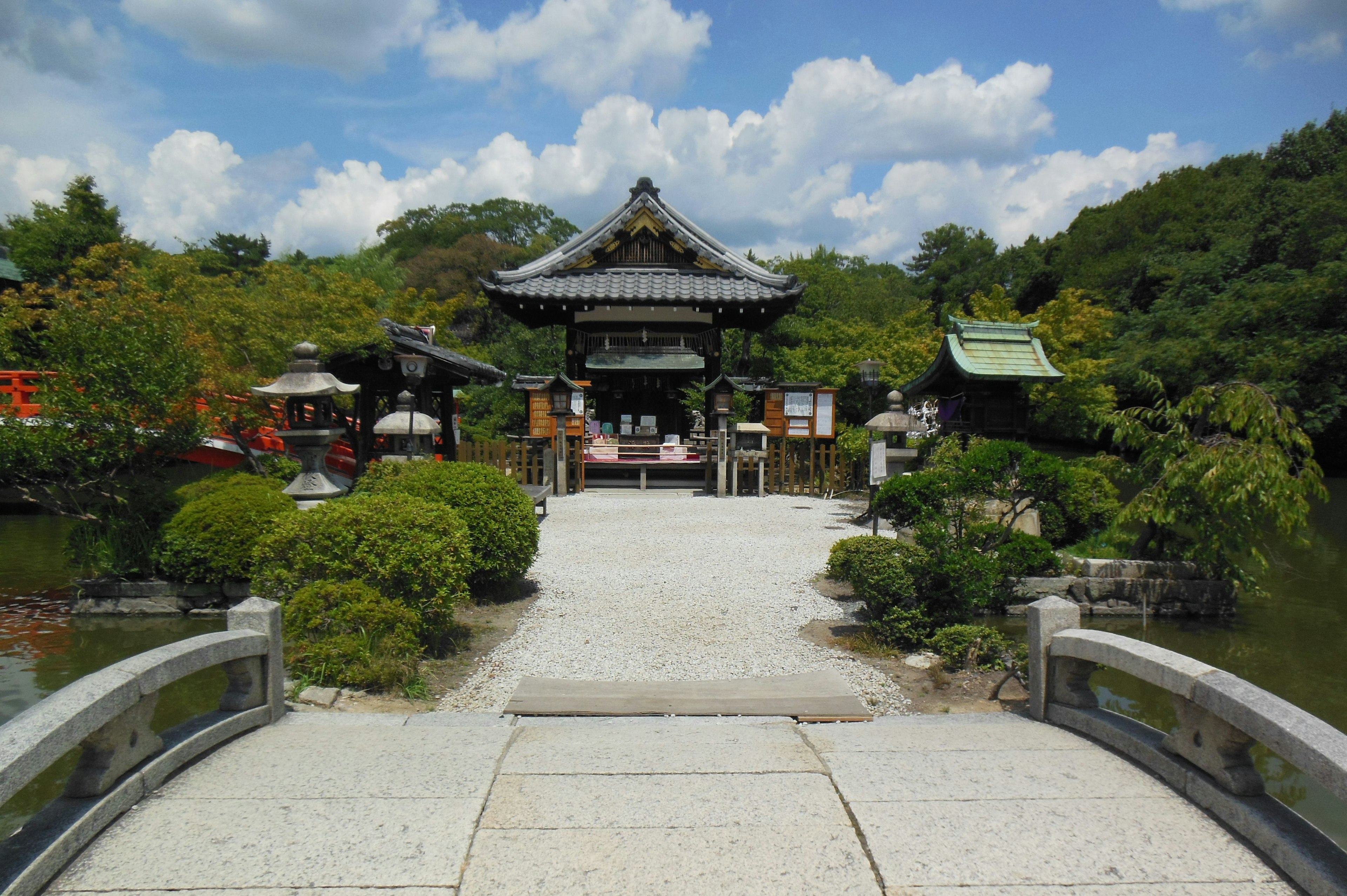 Beautiful Japanese garden scene with a bridge leading to a traditional building surrounded by lush greenery and blue skies