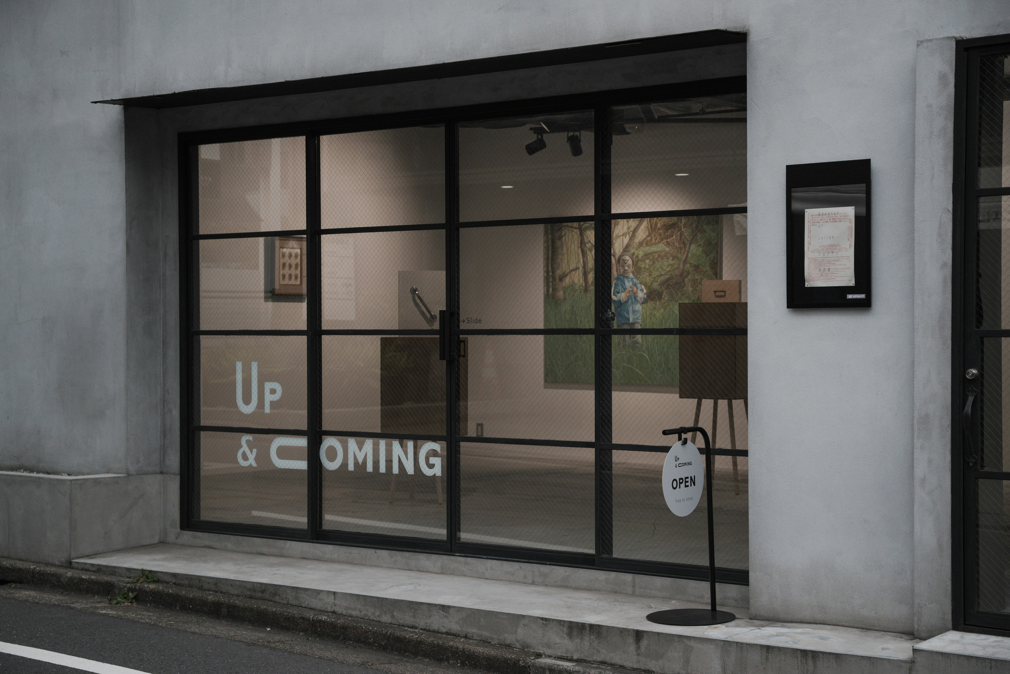 Exterior of an art gallery featuring black-framed glass windows with the words Up & Coming