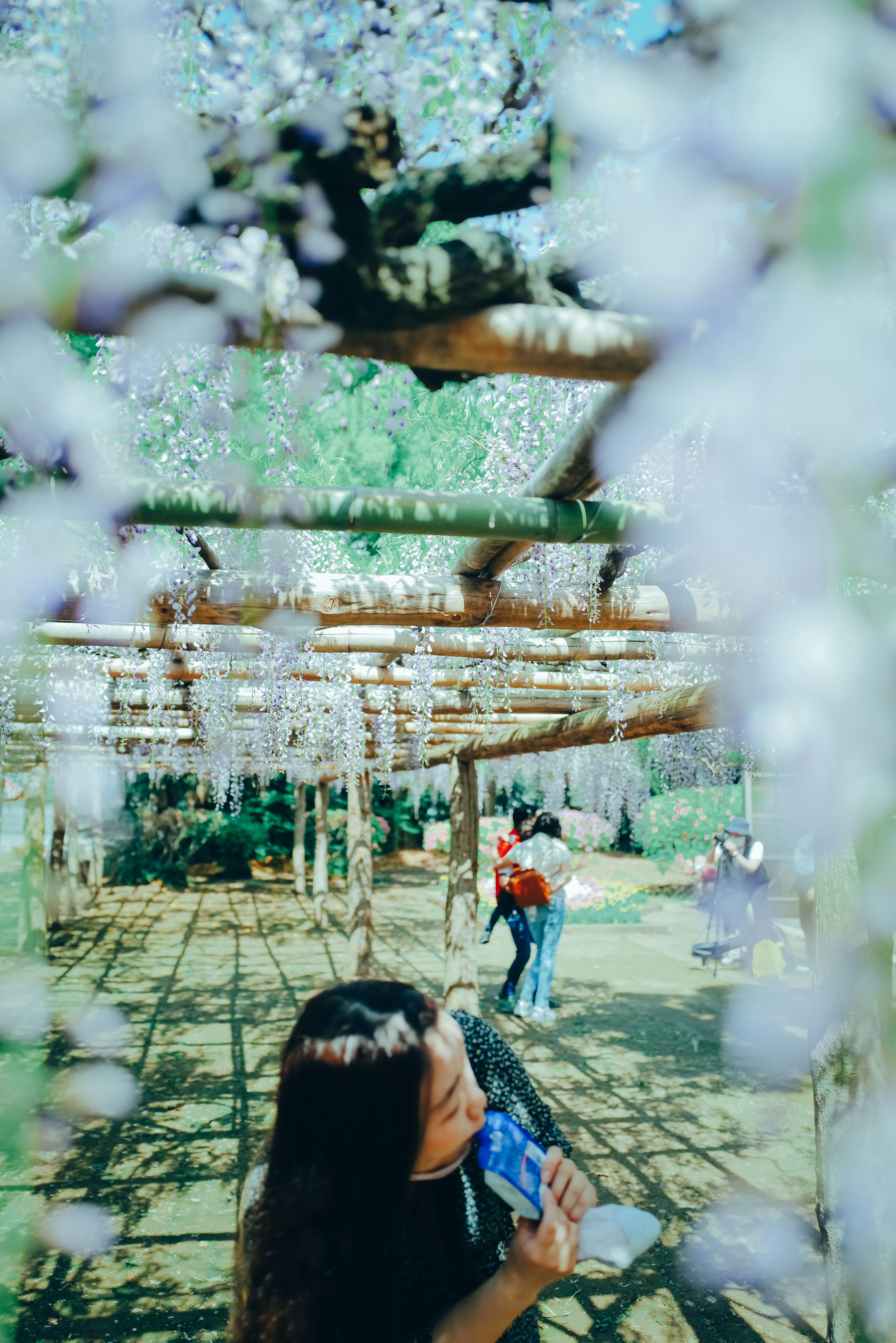 Une femme tenant une boisson bleue sourit sous un arbre avec des fleurs violettes