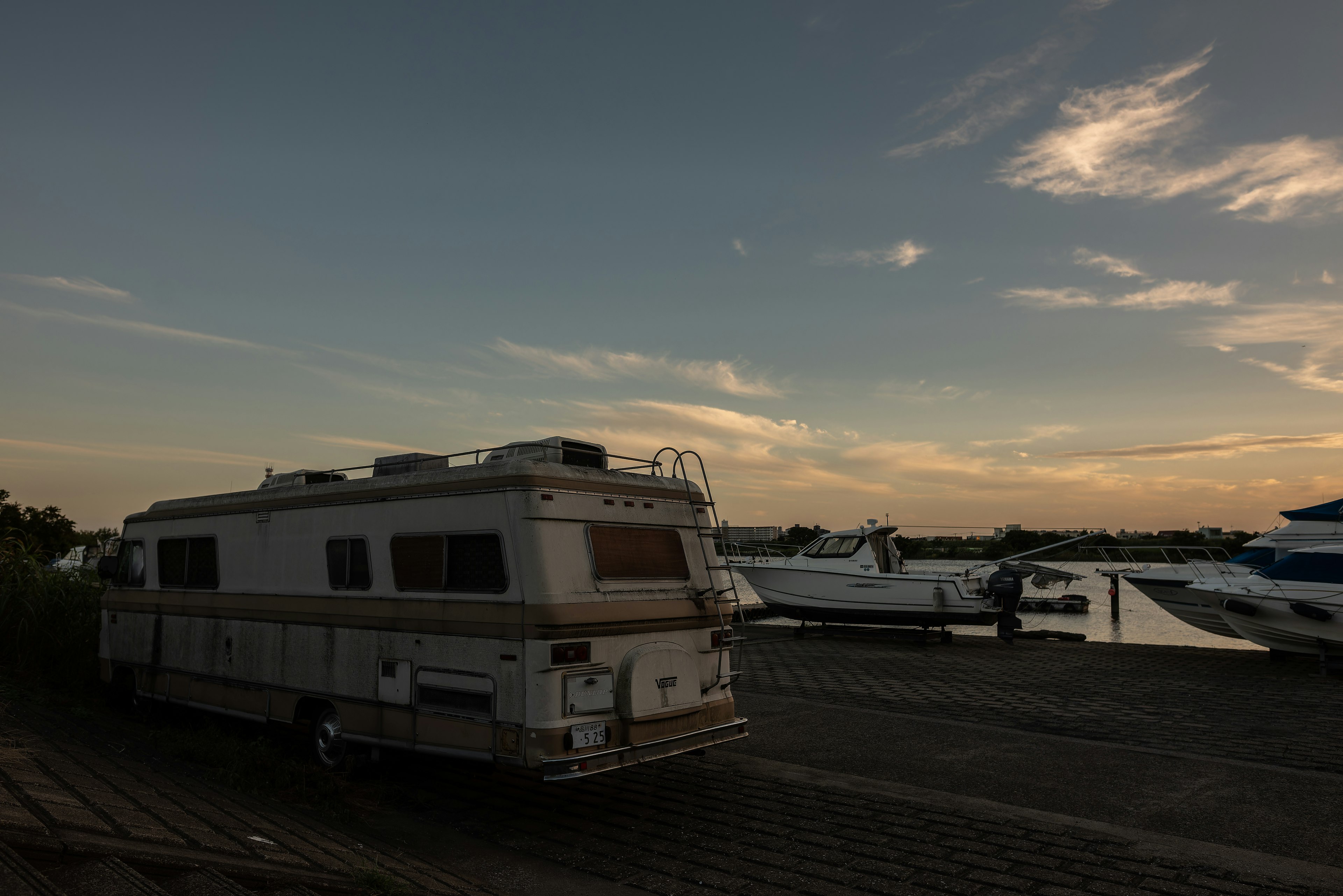 Old camper parked near a marina at sunset with boats in the background