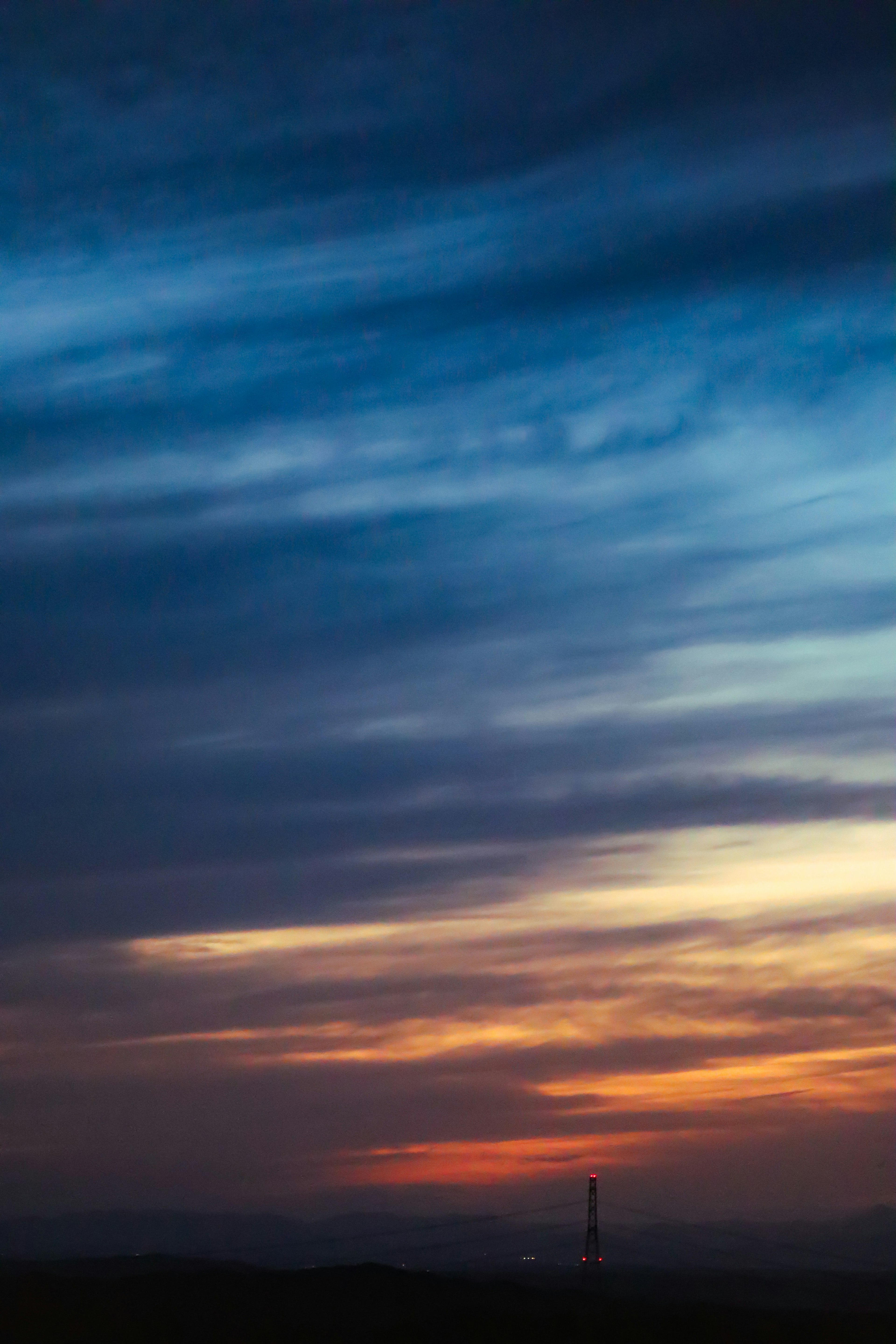 Ein atemberaubender Sonnenuntergangshimmel mit blauen und orangefarbenen Abstufungen, die einen fernen Turm am Horizont silhouettieren