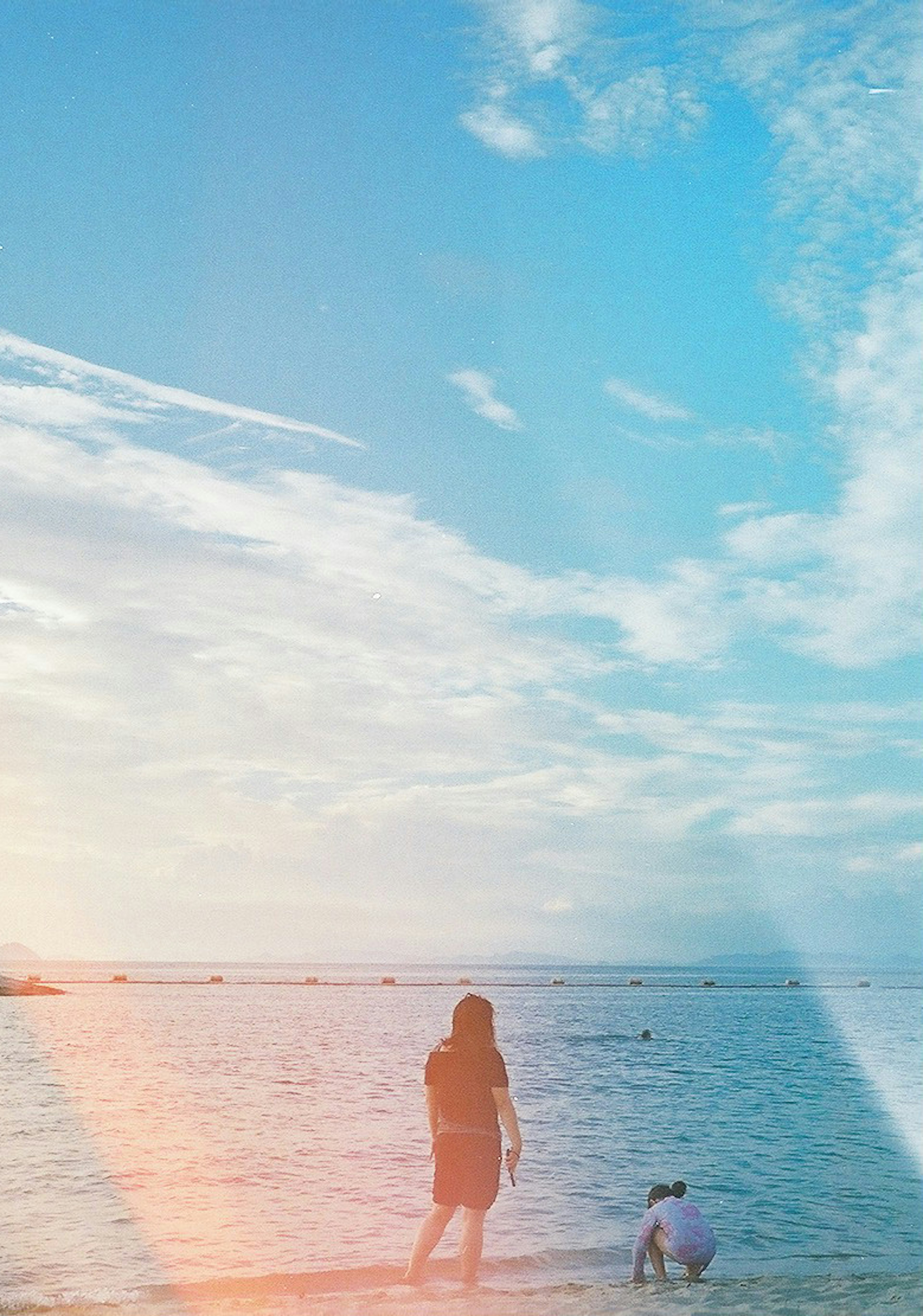 Silhouette eines Erwachsenen und eines Kindes, die am Strand spielen, mit einem schönen blauen Himmel und Wolken