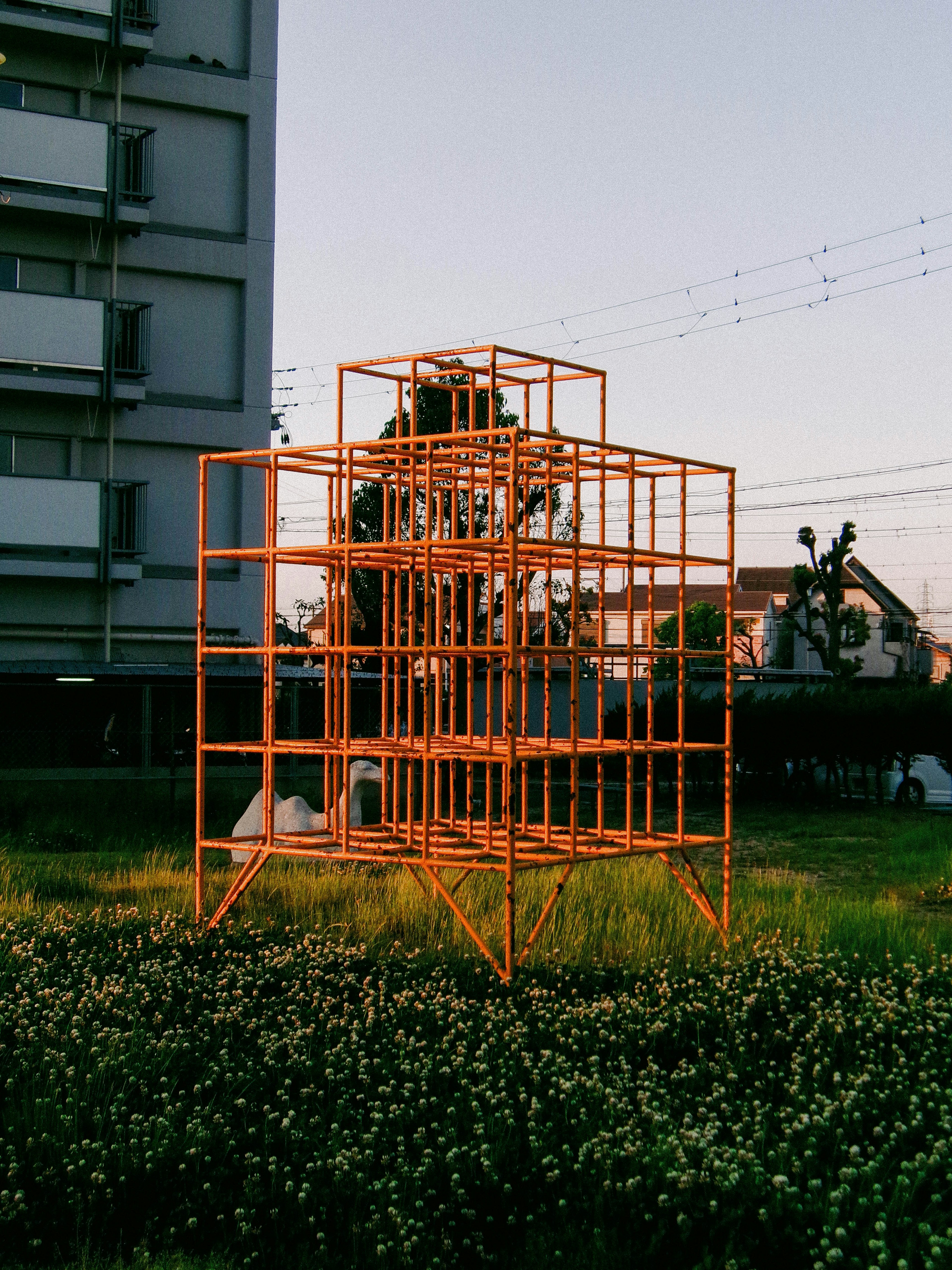 Orange frame structure standing in grass with buildings in the background