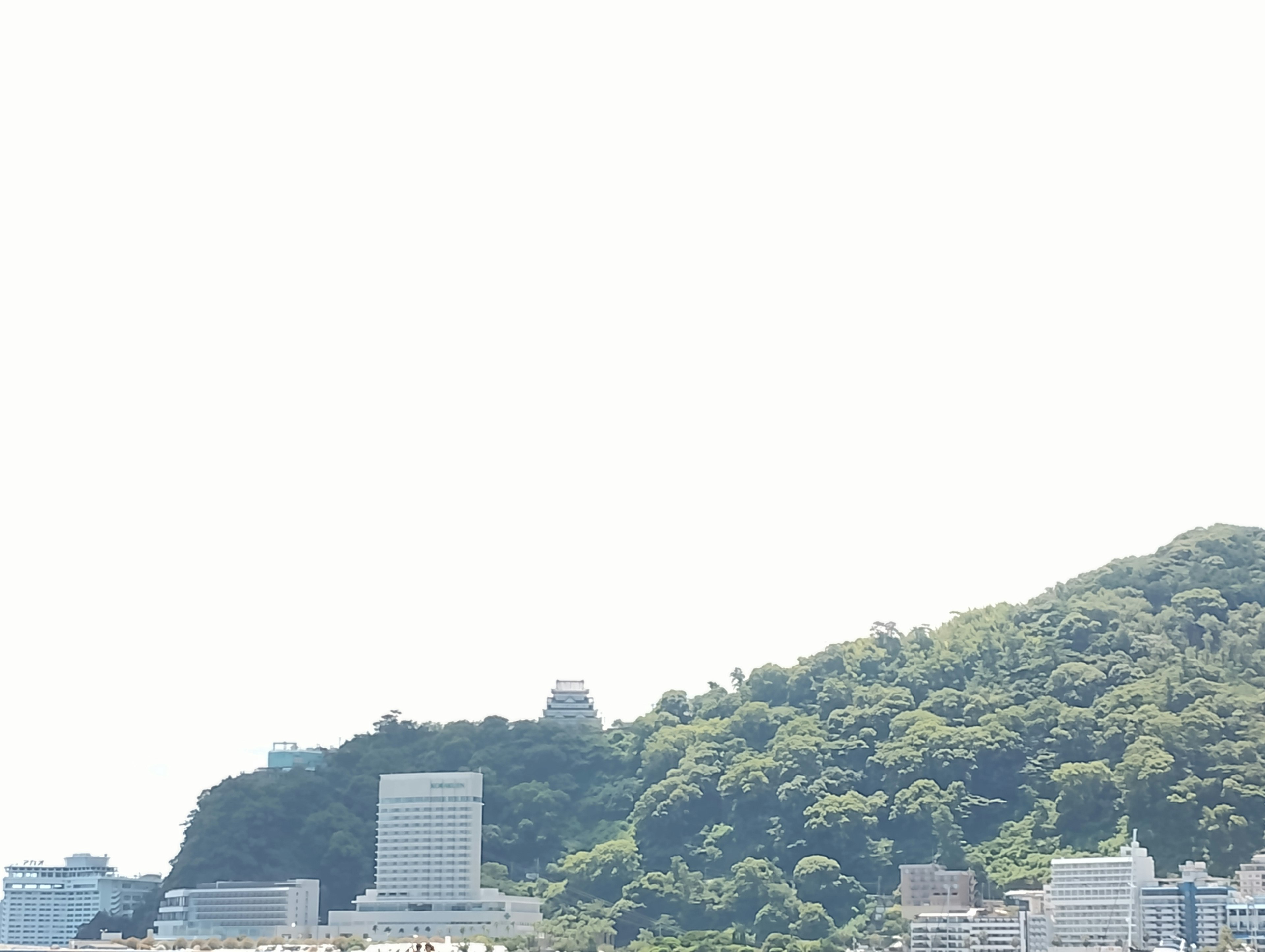 Coastal view featuring lush green hills and modern buildings under a clear blue sky