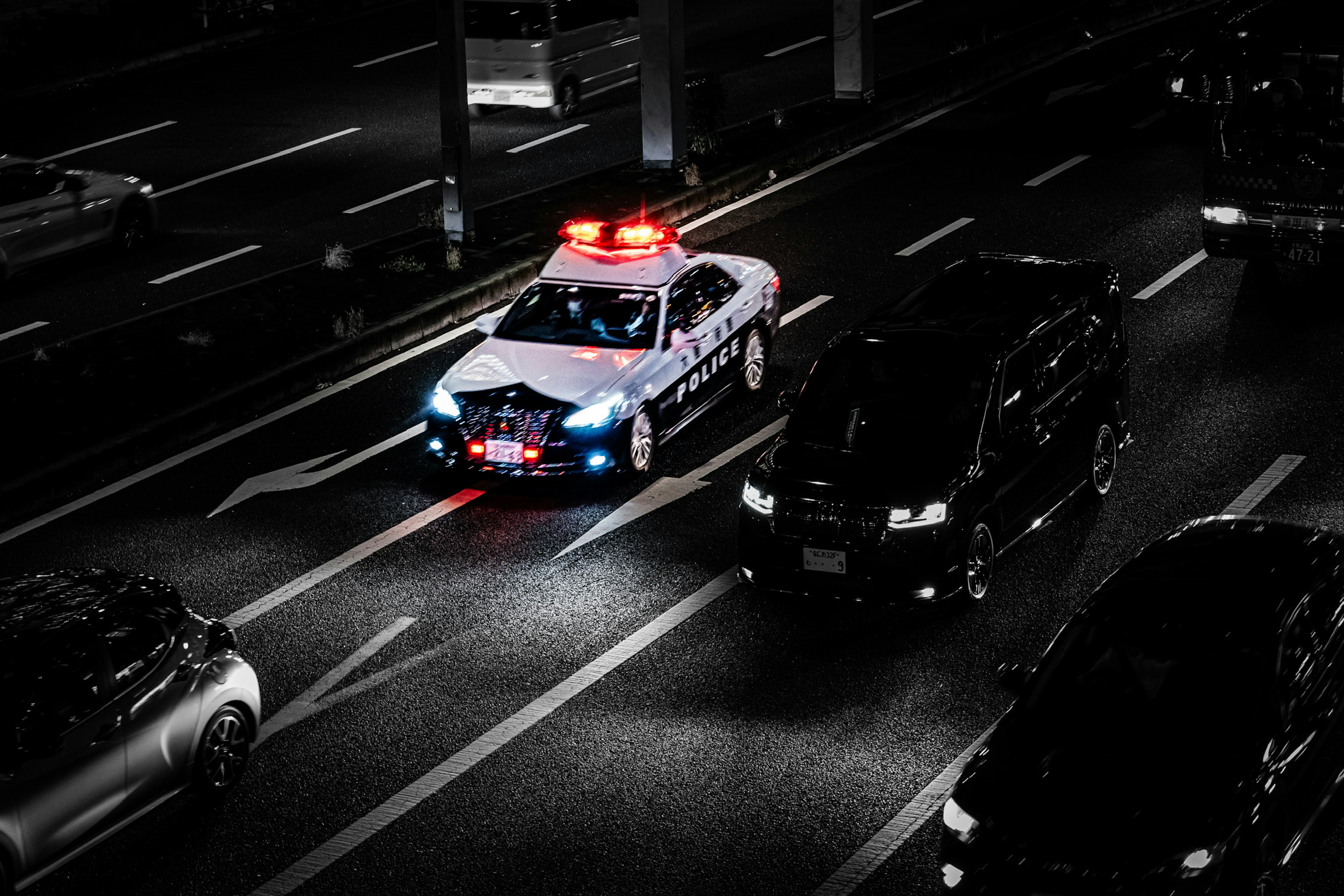 A police car with flashing red and blue lights navigating through traffic on a night road