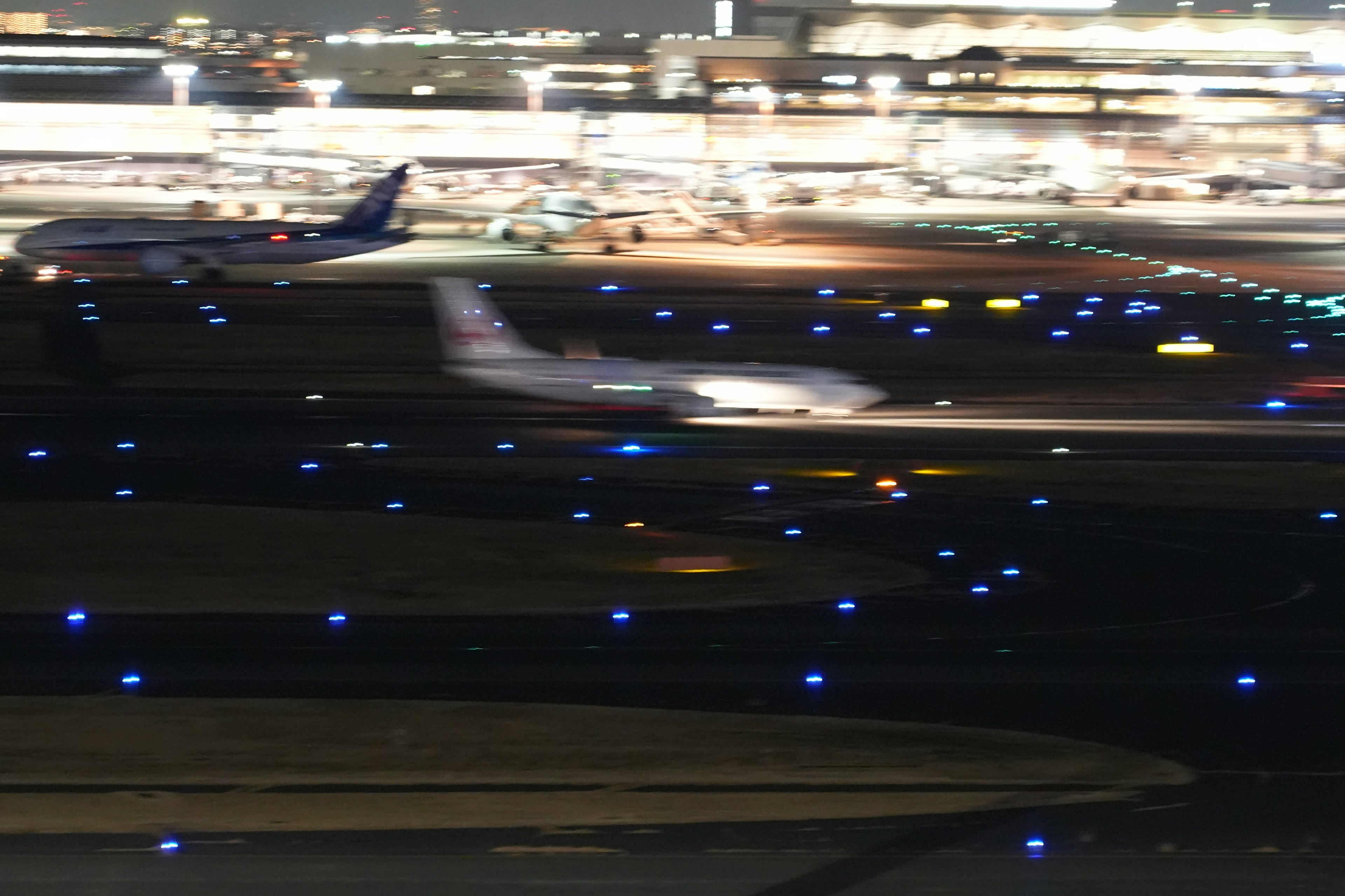 An airplane taxiing on a runway at night with blue taxiway lights