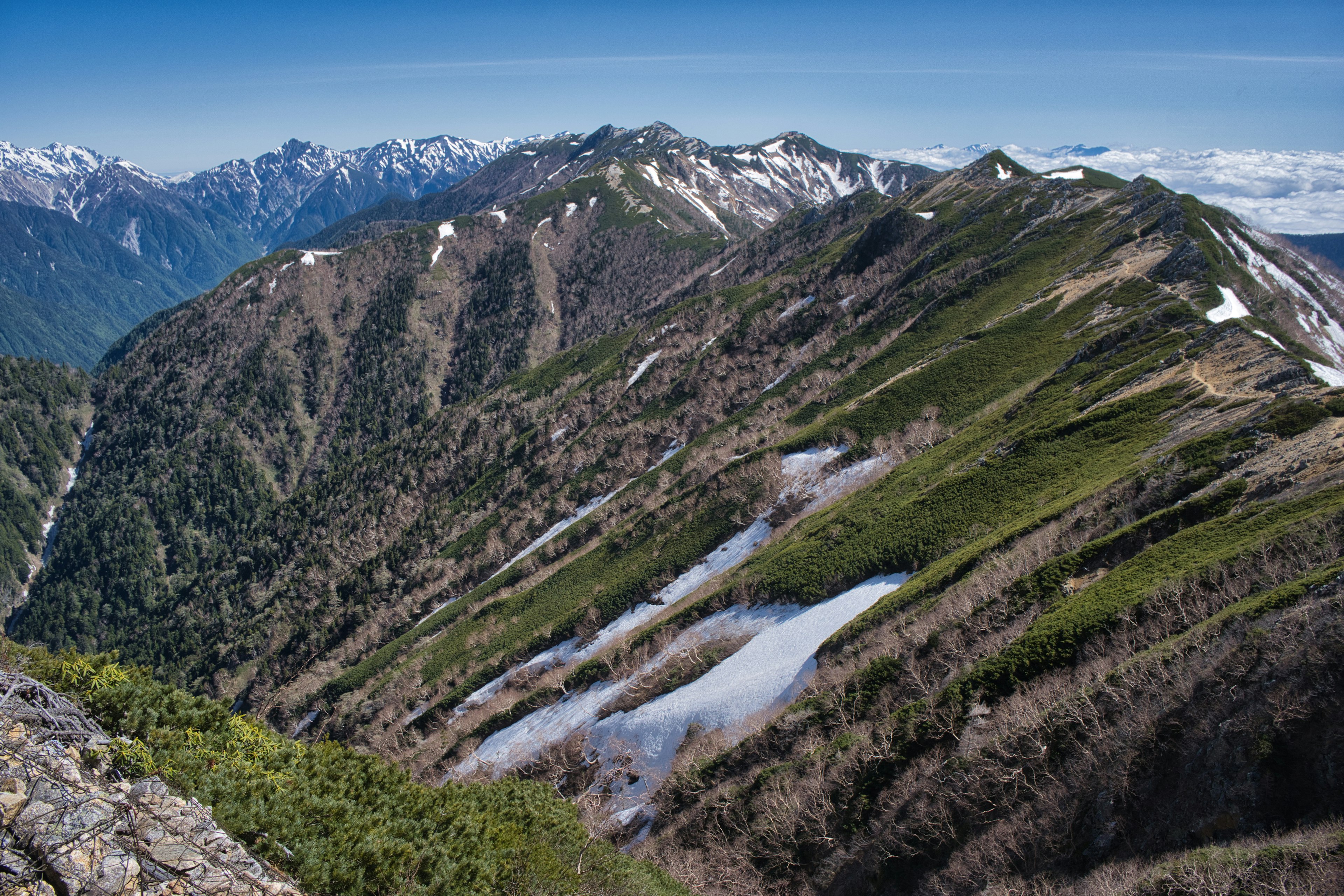 Malersiche Berglandschaft mit grünen Hängen und Schneeresten unter einem klaren blauen Himmel