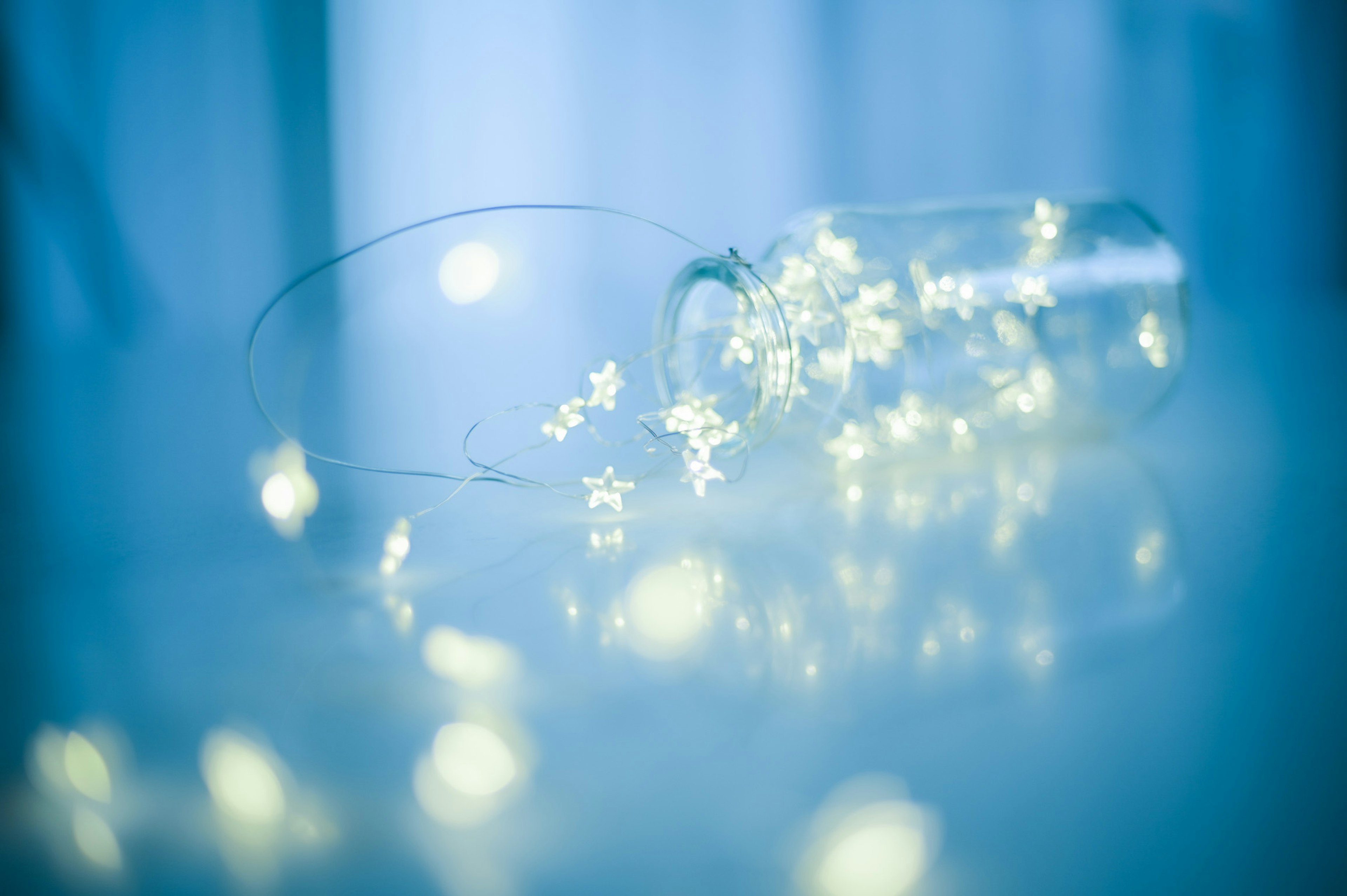 A glass jar spilling tiny glowing flower decorations on a blue background