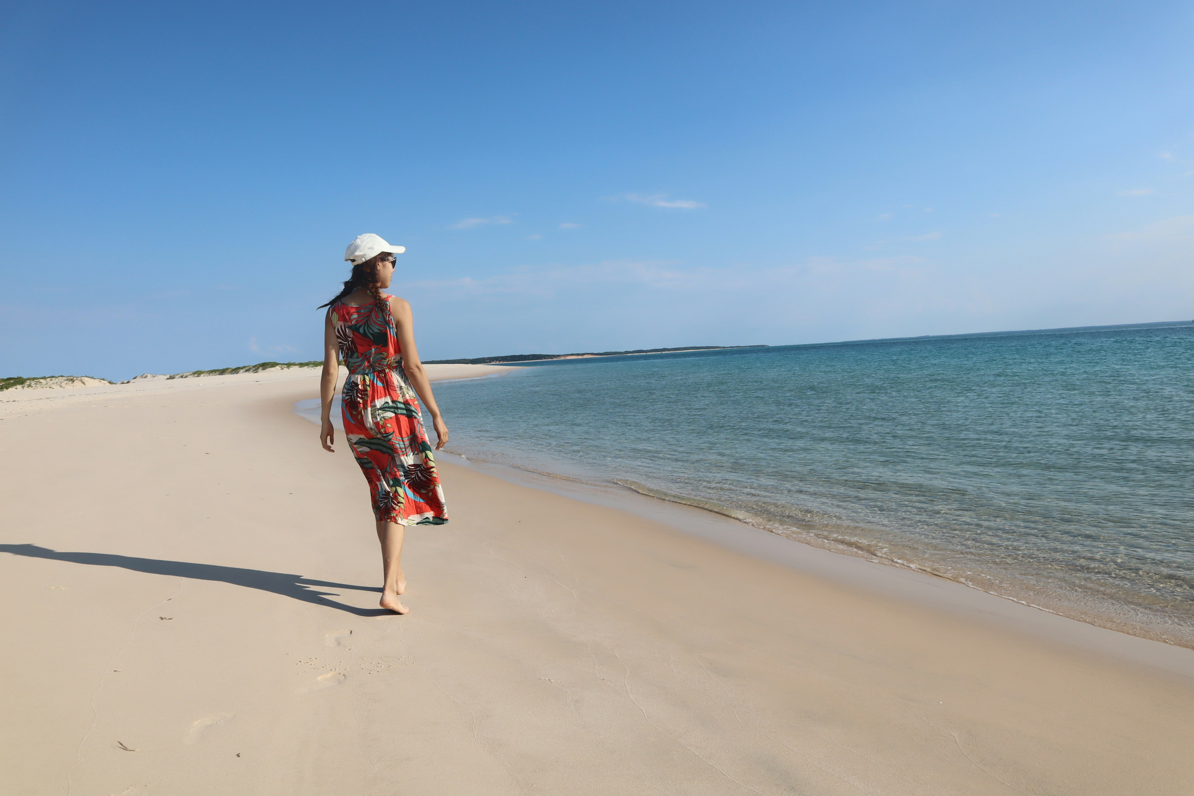 Woman walking on the beach with blue sky and ocean, white sandy shore