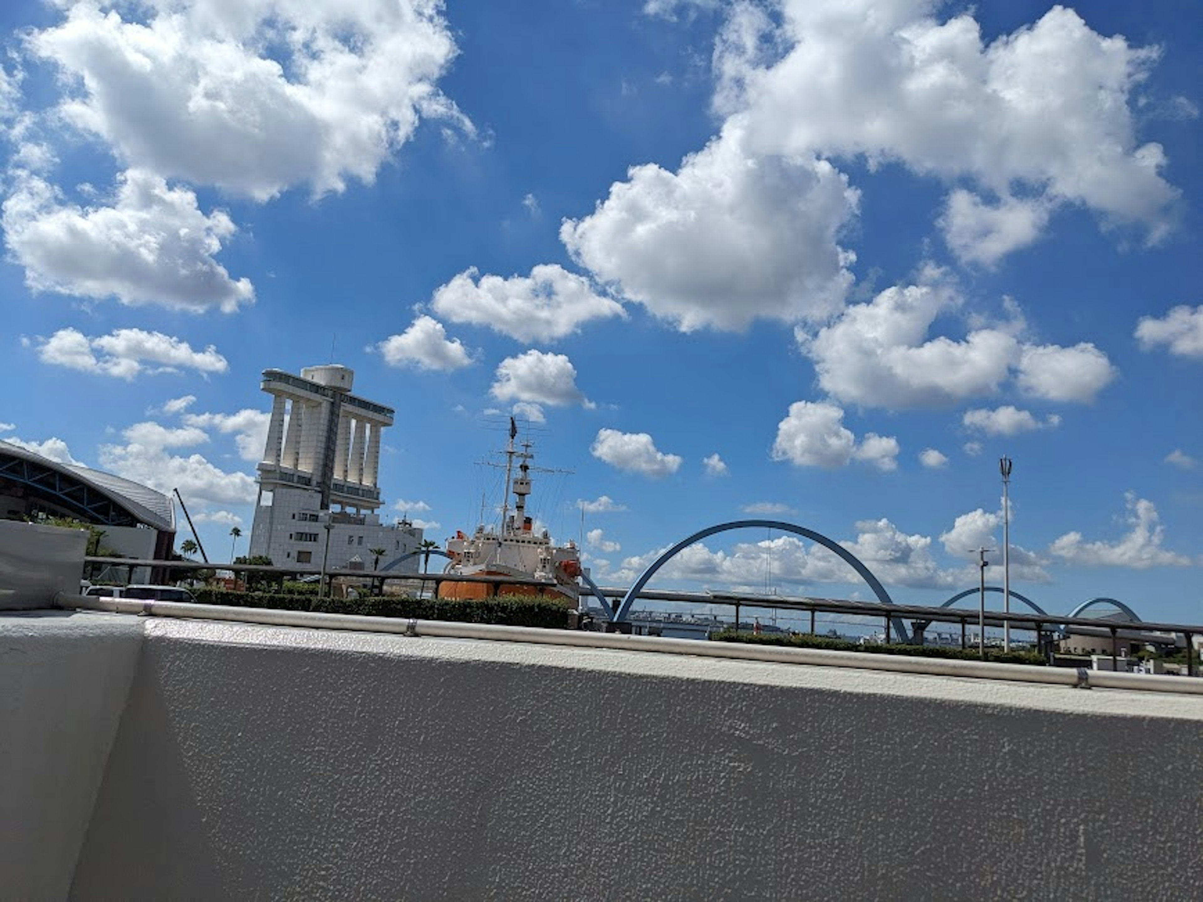 Un paisaje con cielo azul y nubes blancas esponjosas, edificios y un puente en arco