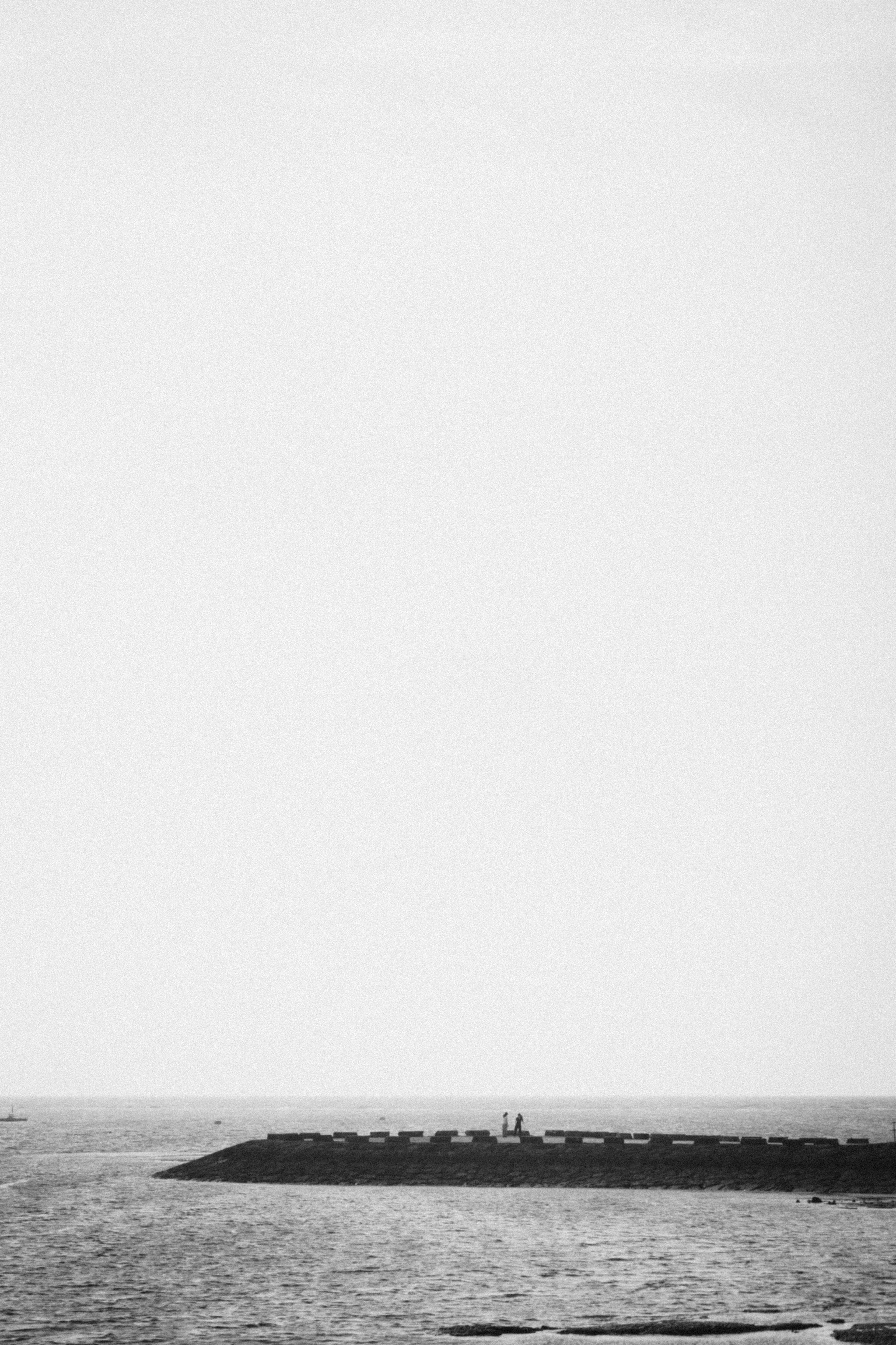 Black and white seascape featuring a jetty with distant figures