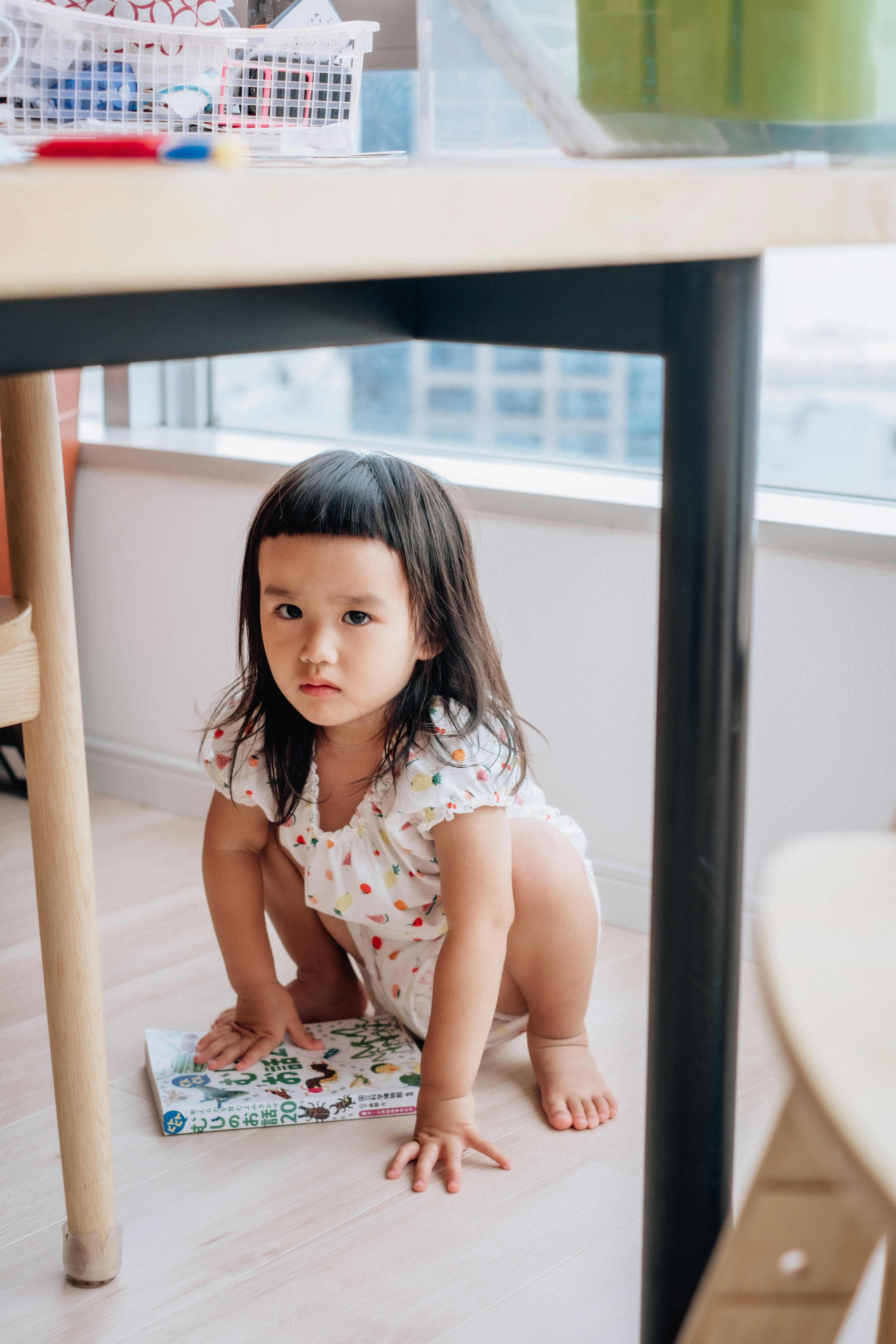 テーブルの下で座っている子供の写真 短い髪で白い服を着ている