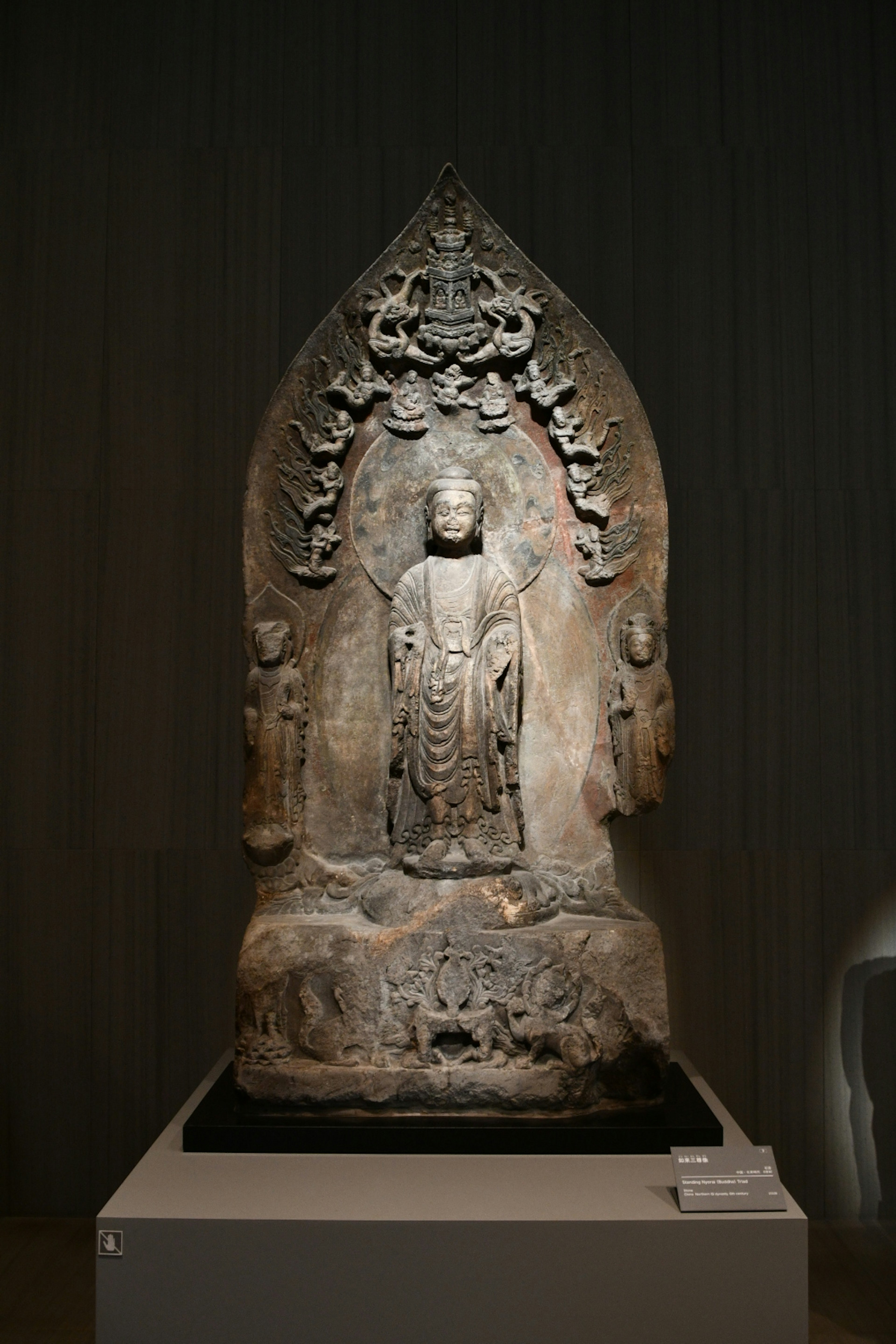 A carved Buddha statue stands centrally with smaller figures surrounding it