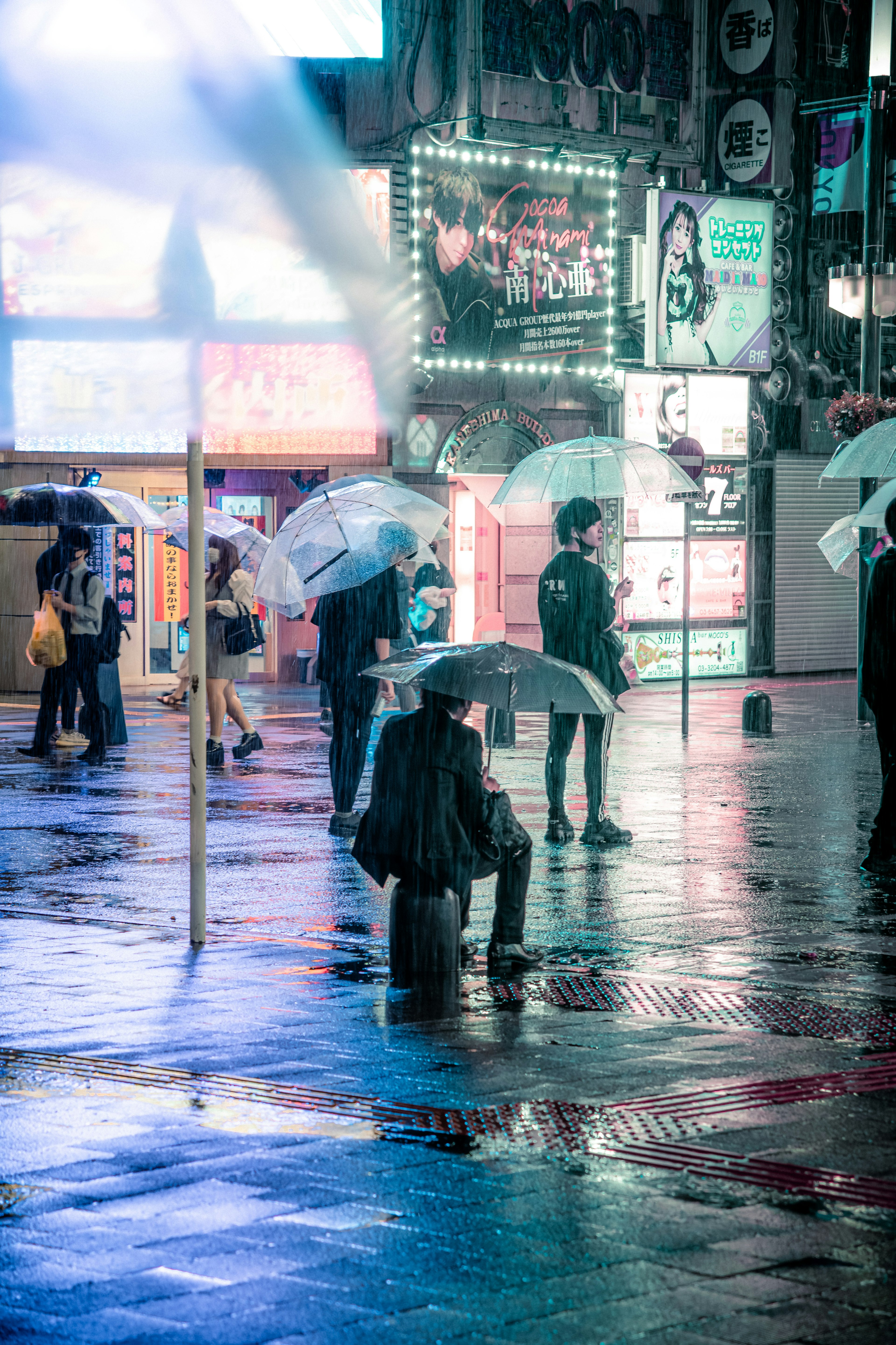 雨の中、傘を持つ人々が立っている街の風景