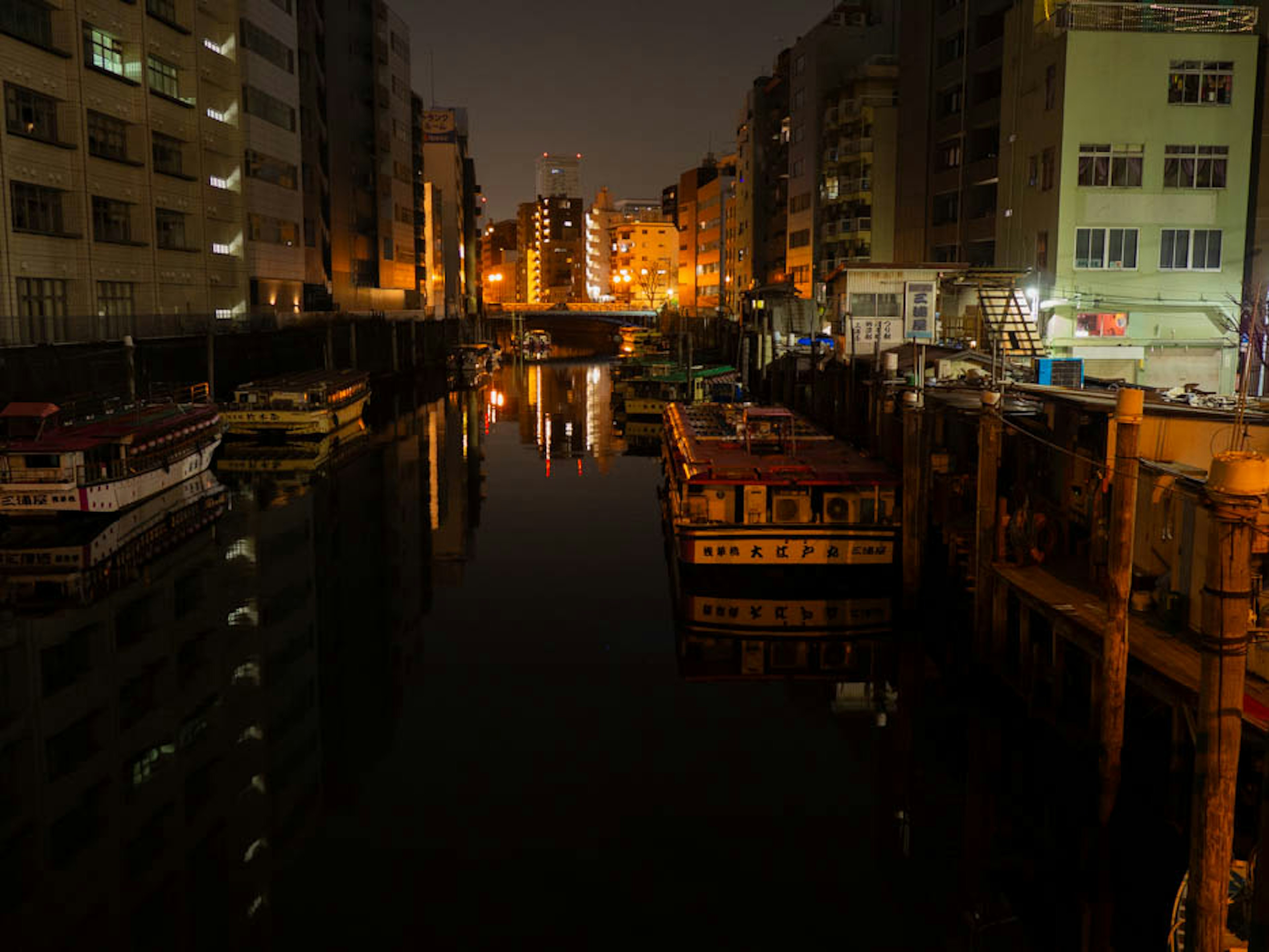 Vue nocturne de bateaux sur un canal avec des reflets de bâtiments