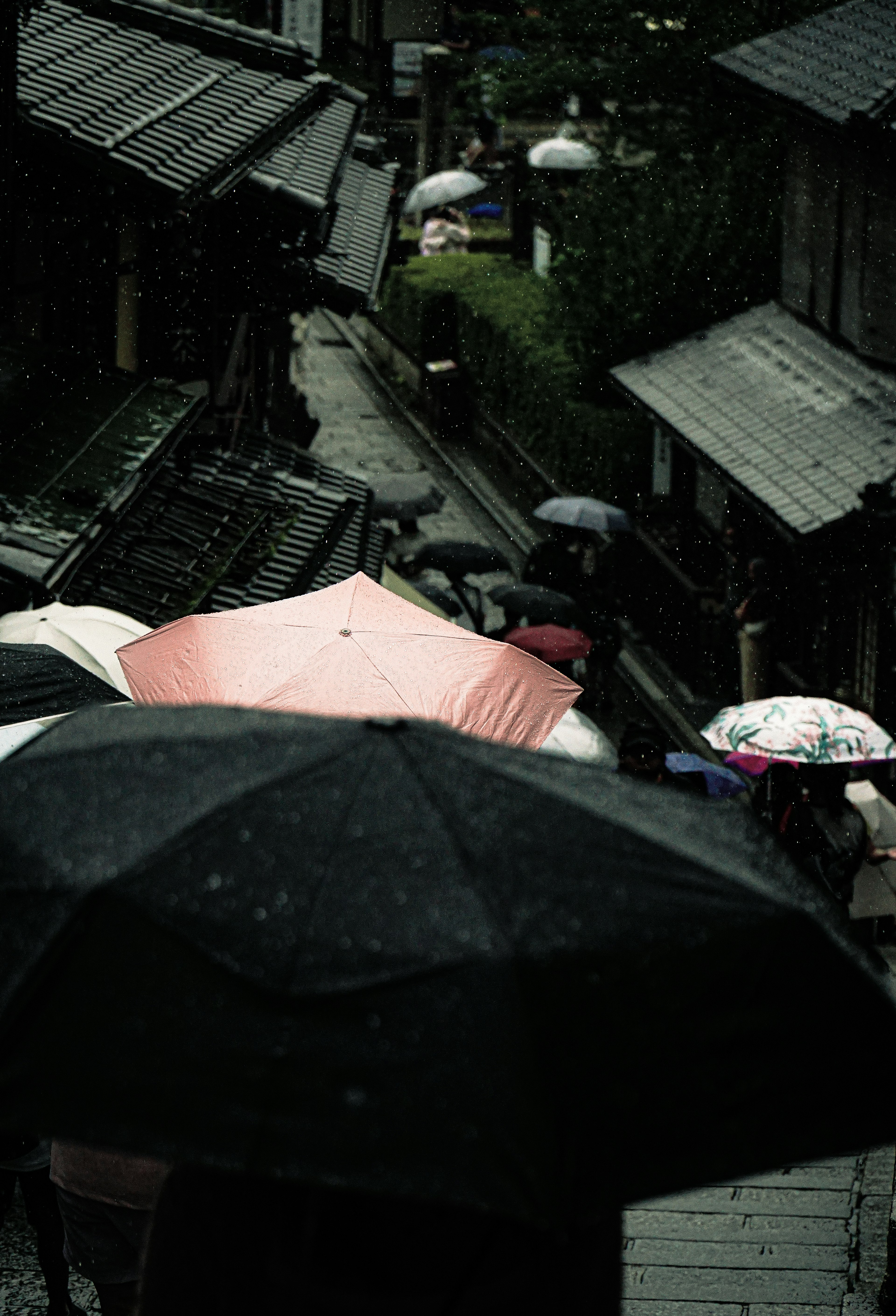 雨の中で傘をさした人々が行き交う古い街並みの風景