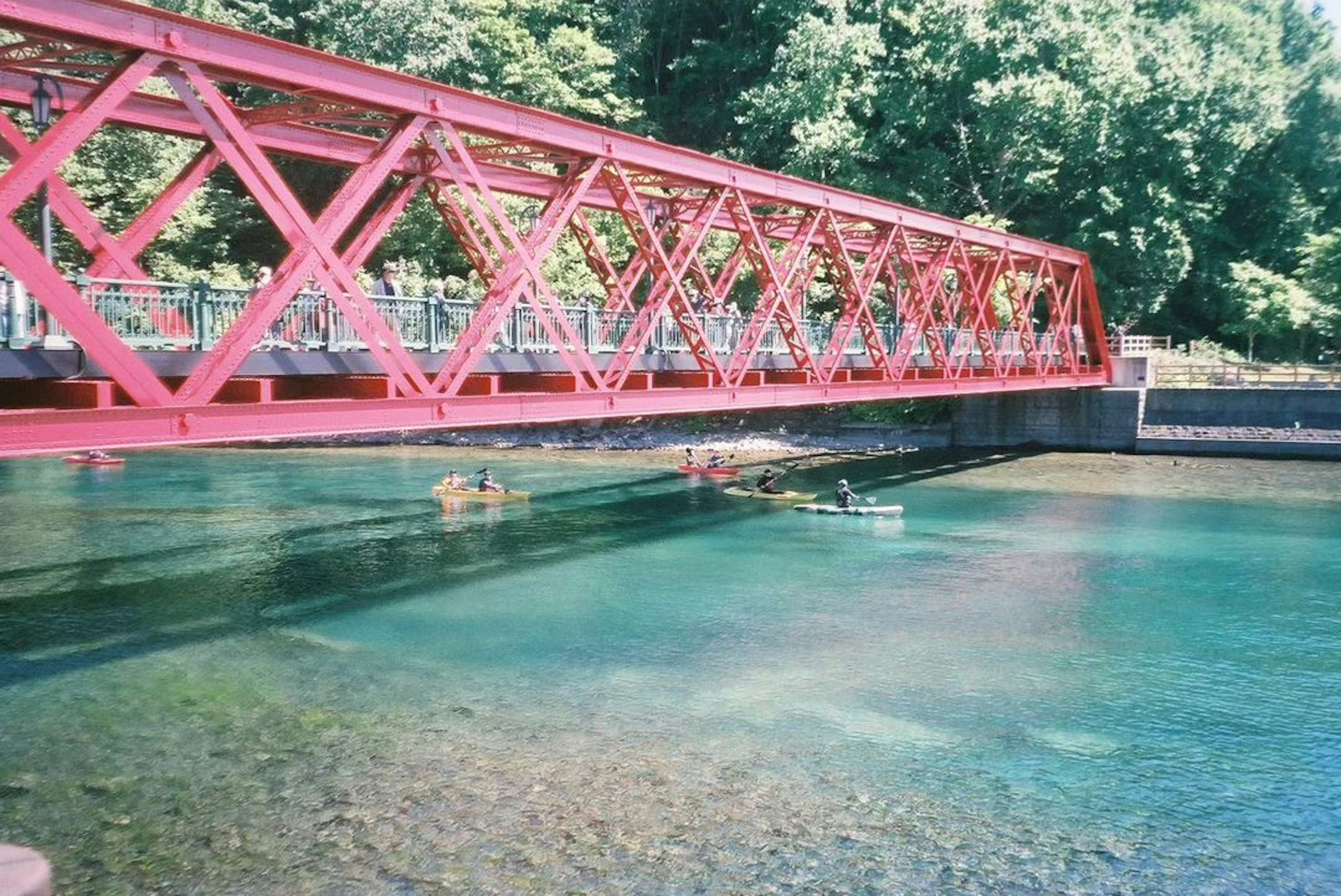 Sebuah jembatan truss merah cerah membentang di atas air jernih