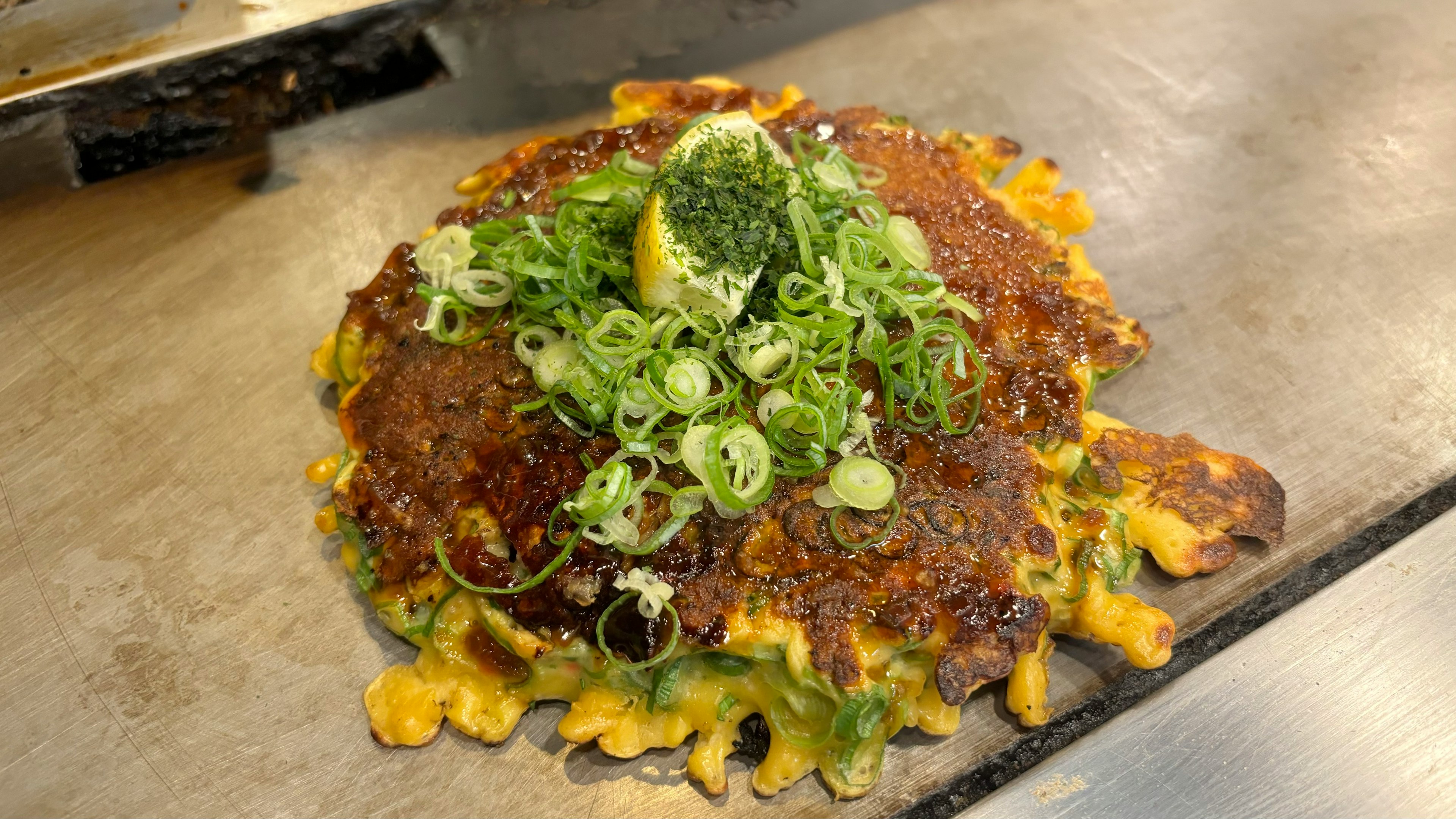 Okonomiyaki dengan daun bawang dan lemon di atas panggangan panas