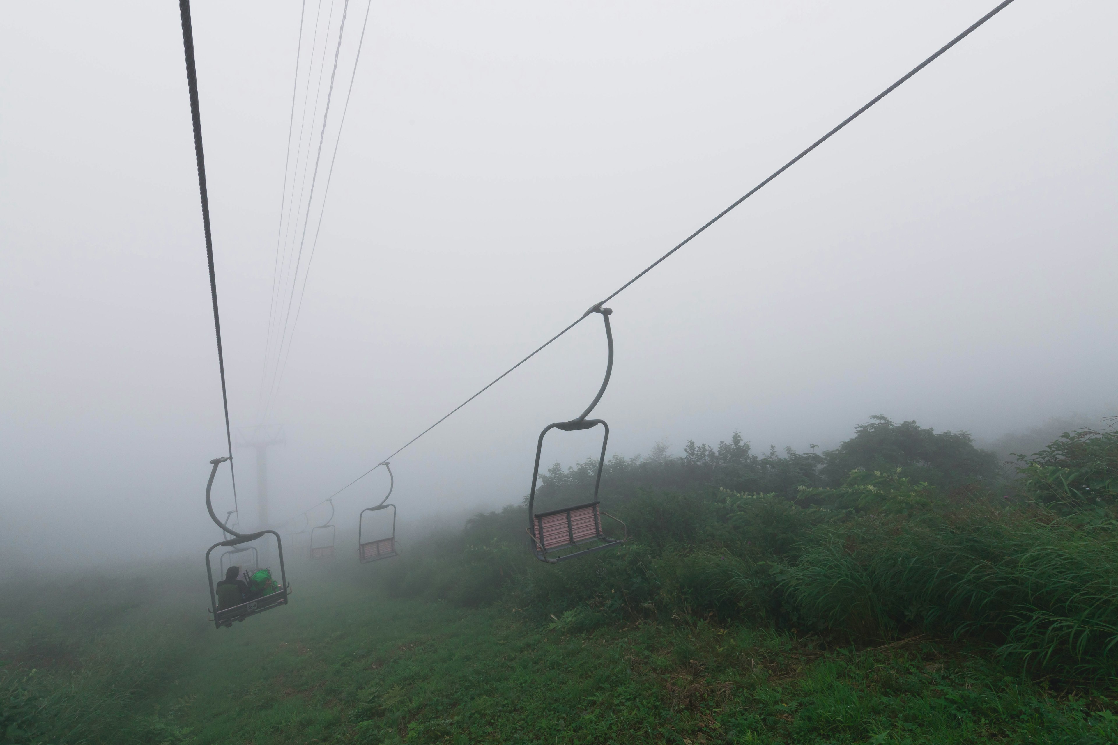 被雾笼罩的滑雪缆车和下面的绿色草地