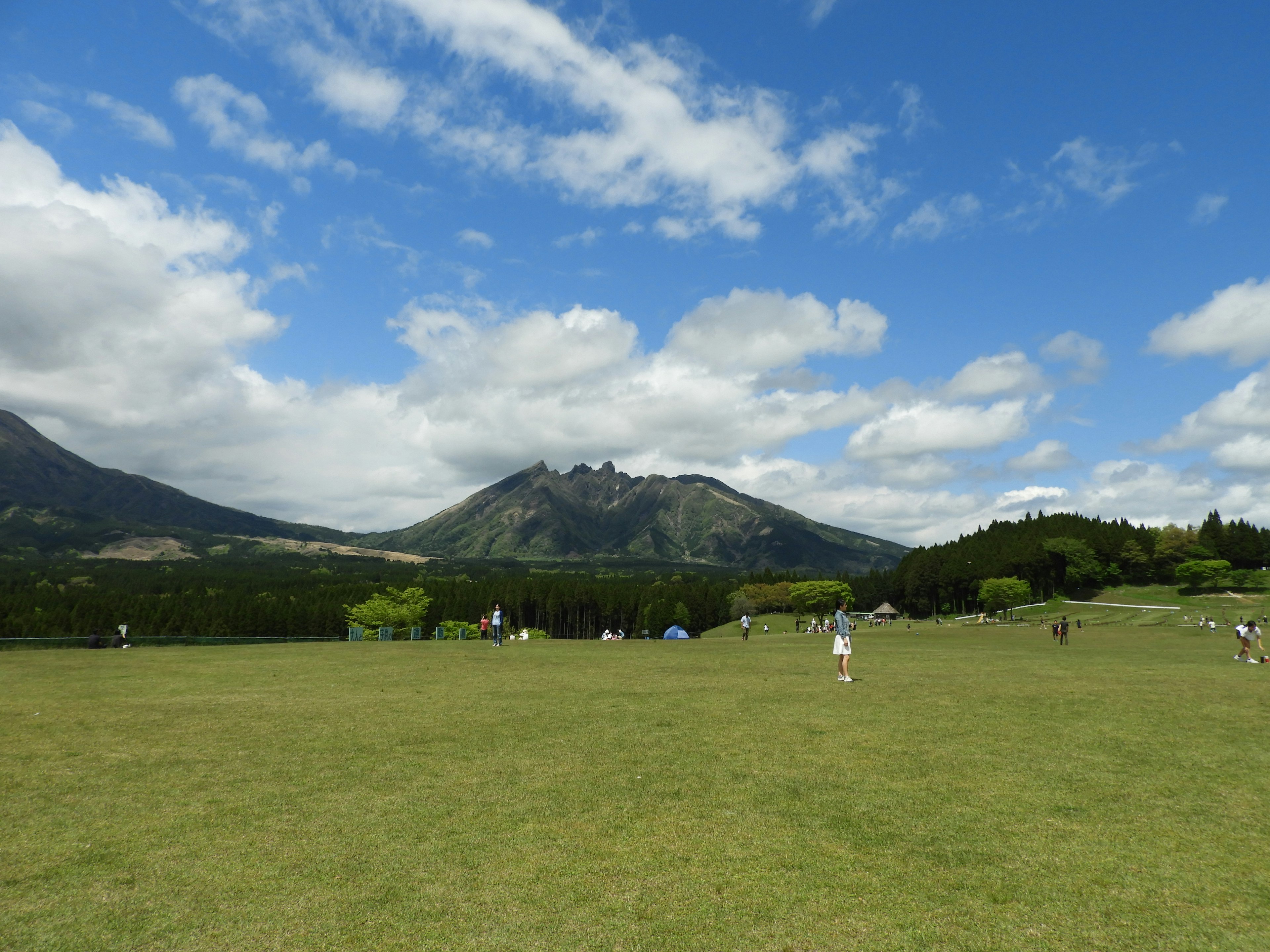 Vista escénica de montañas bajo un cielo azul con nubes esponjosas y un campo verde