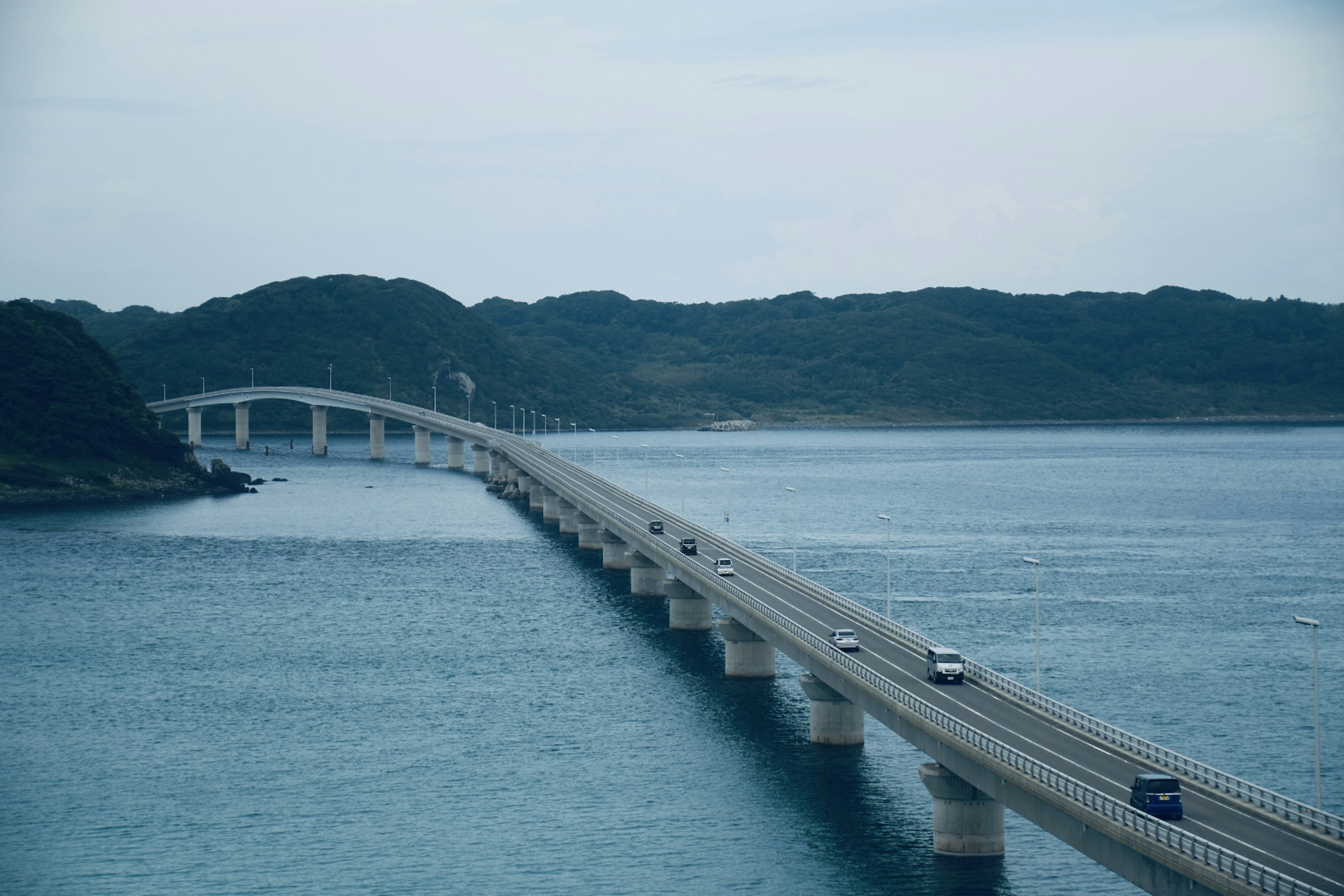 Bridge spanning blue water with green hills in the background