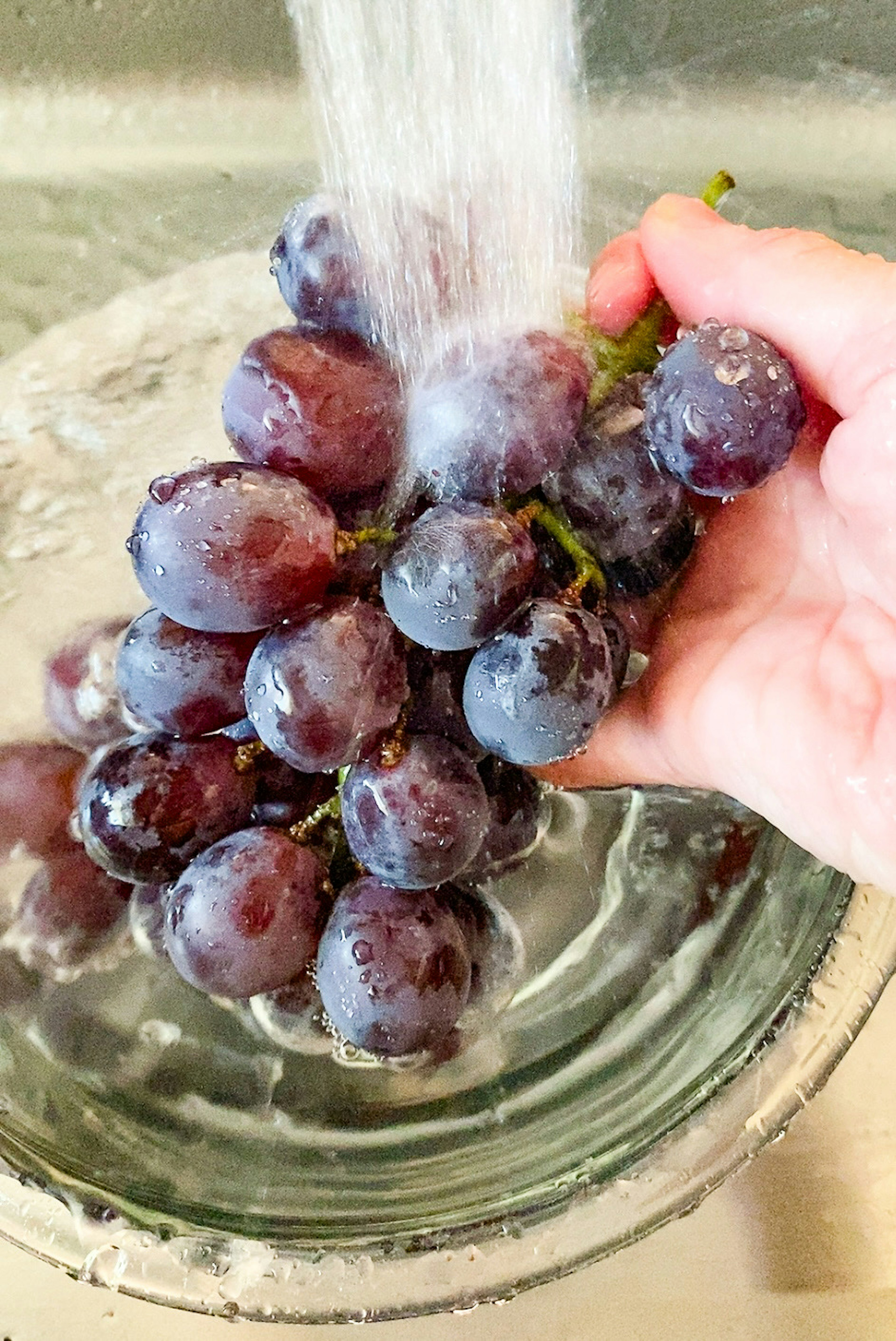 Mano che tiene un grappolo d'uva sotto l'acqua corrente