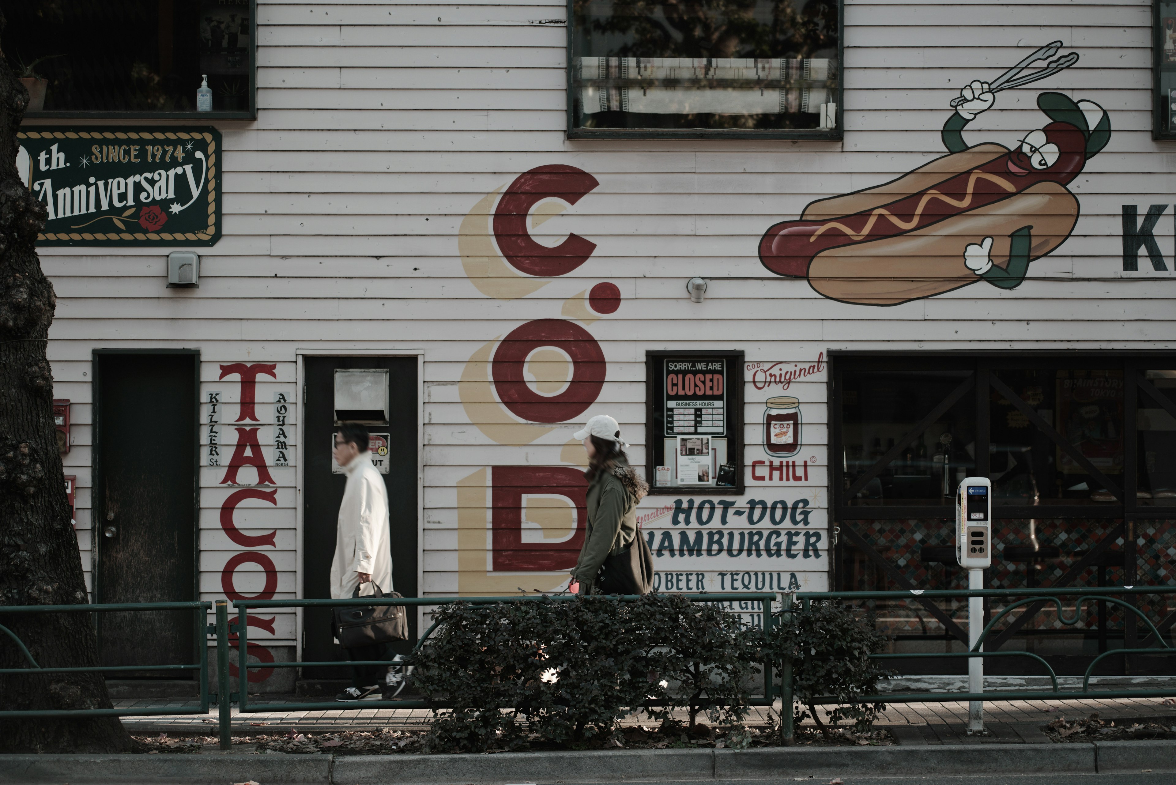 Deux personnes devant un restaurant avec une signalétique colorée incluant des tacos et des hot-dogs