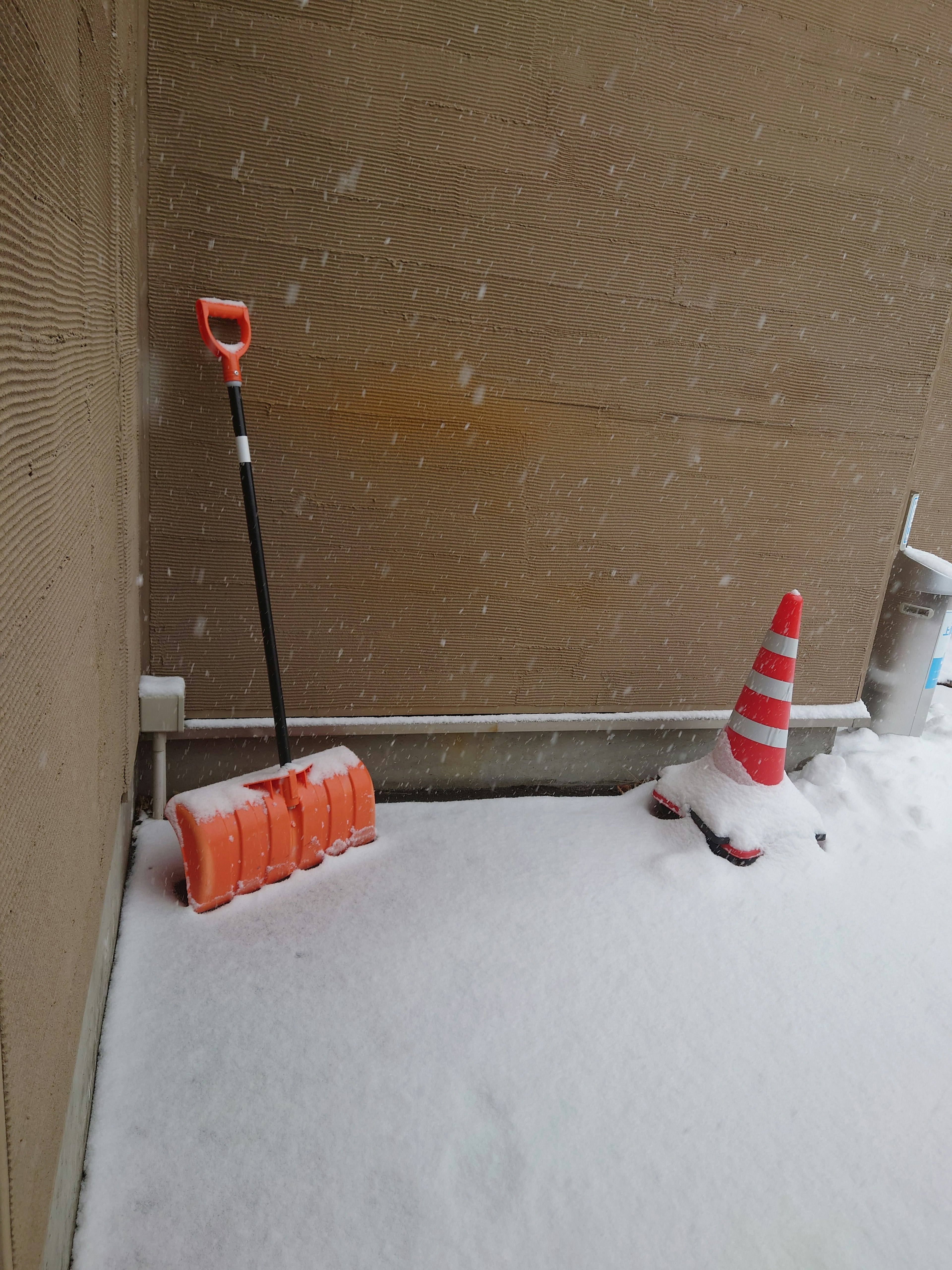 Orange snow shovel and traffic cone in a snowy corner