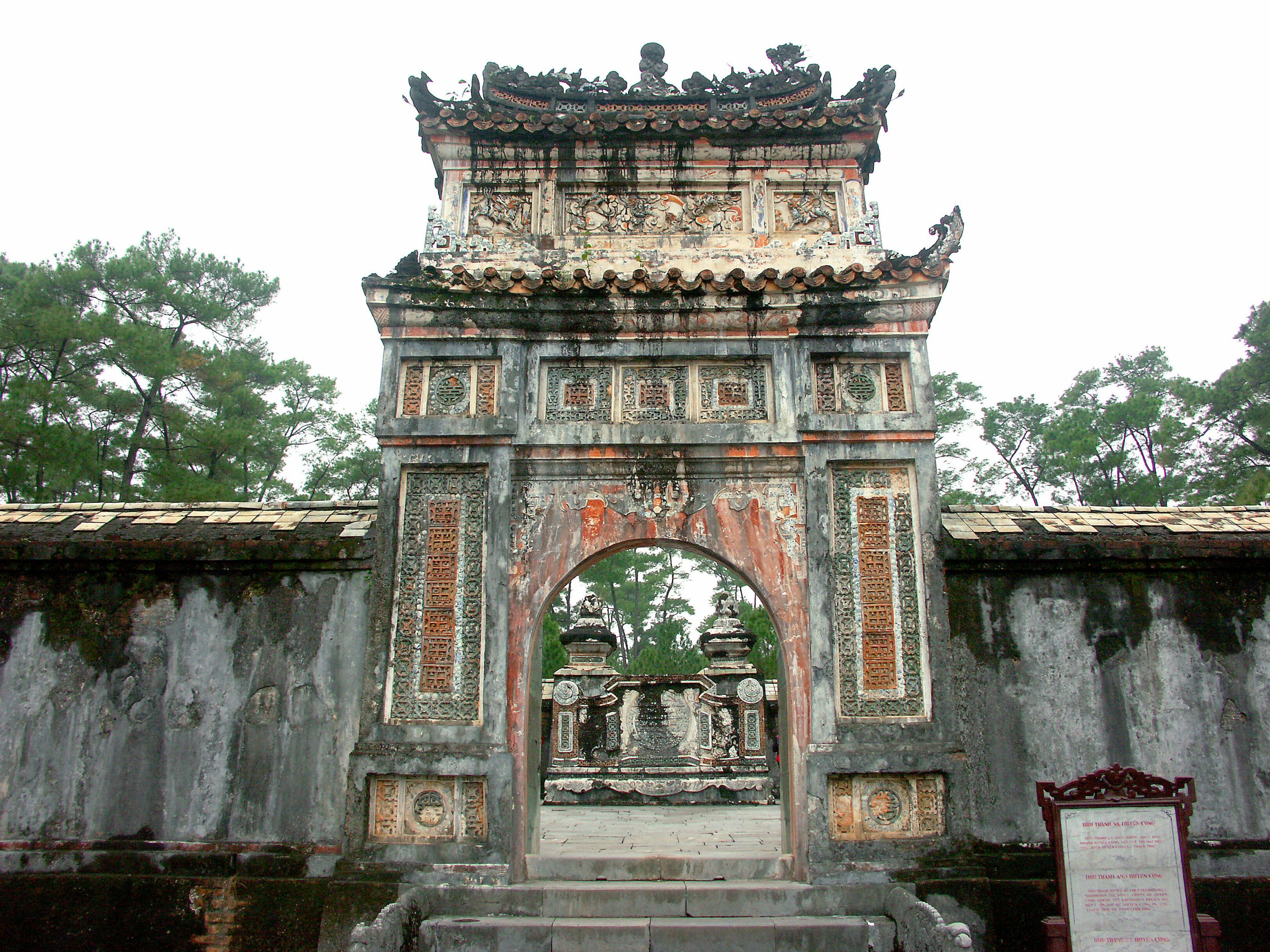 Porte ancienne d'un temple avec des sculptures fanées entourée d'arbres verts