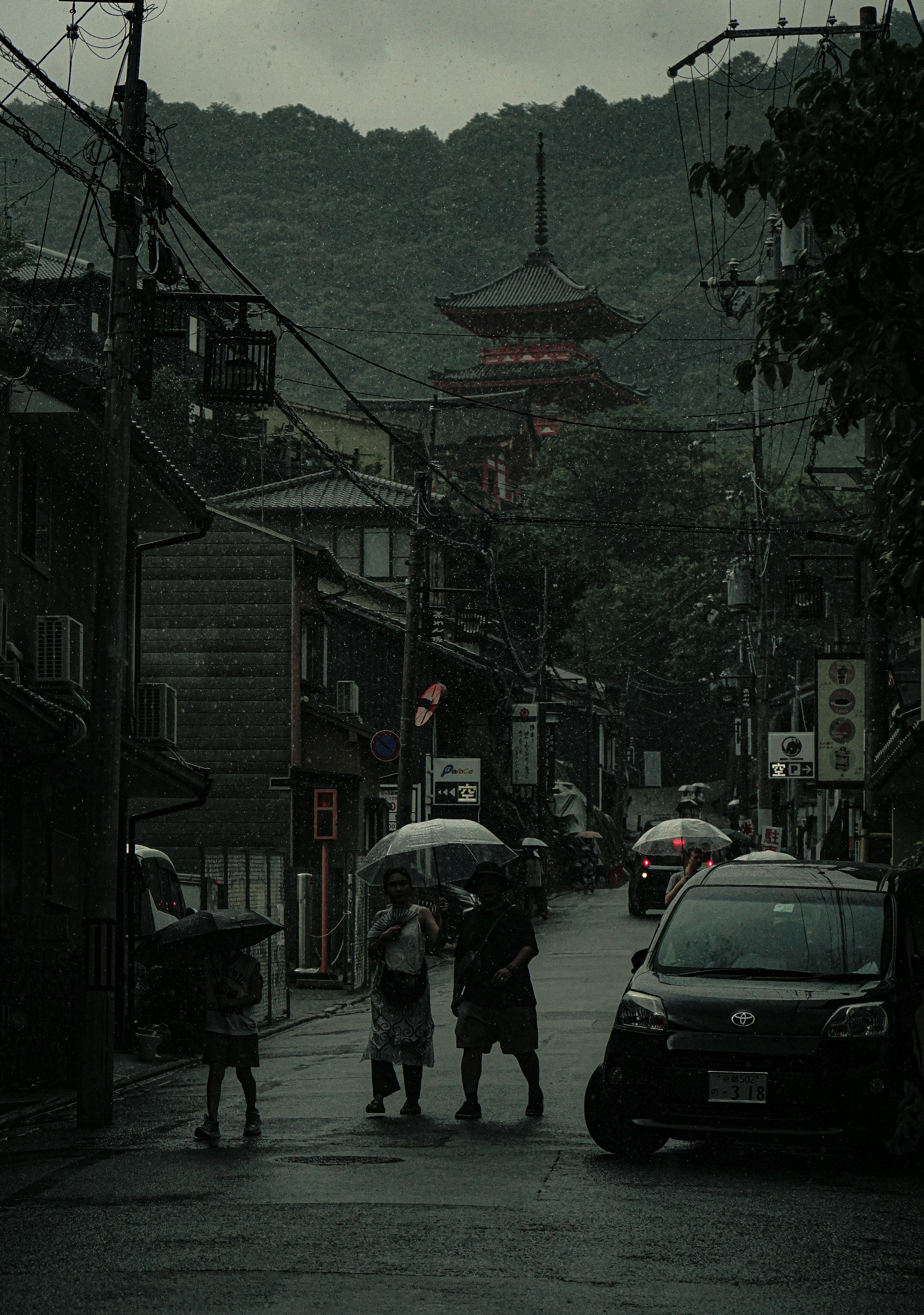 Silhouette de personnes avec des parapluies dans une rue pluvieuse avec une vieille pagode en arrière-plan