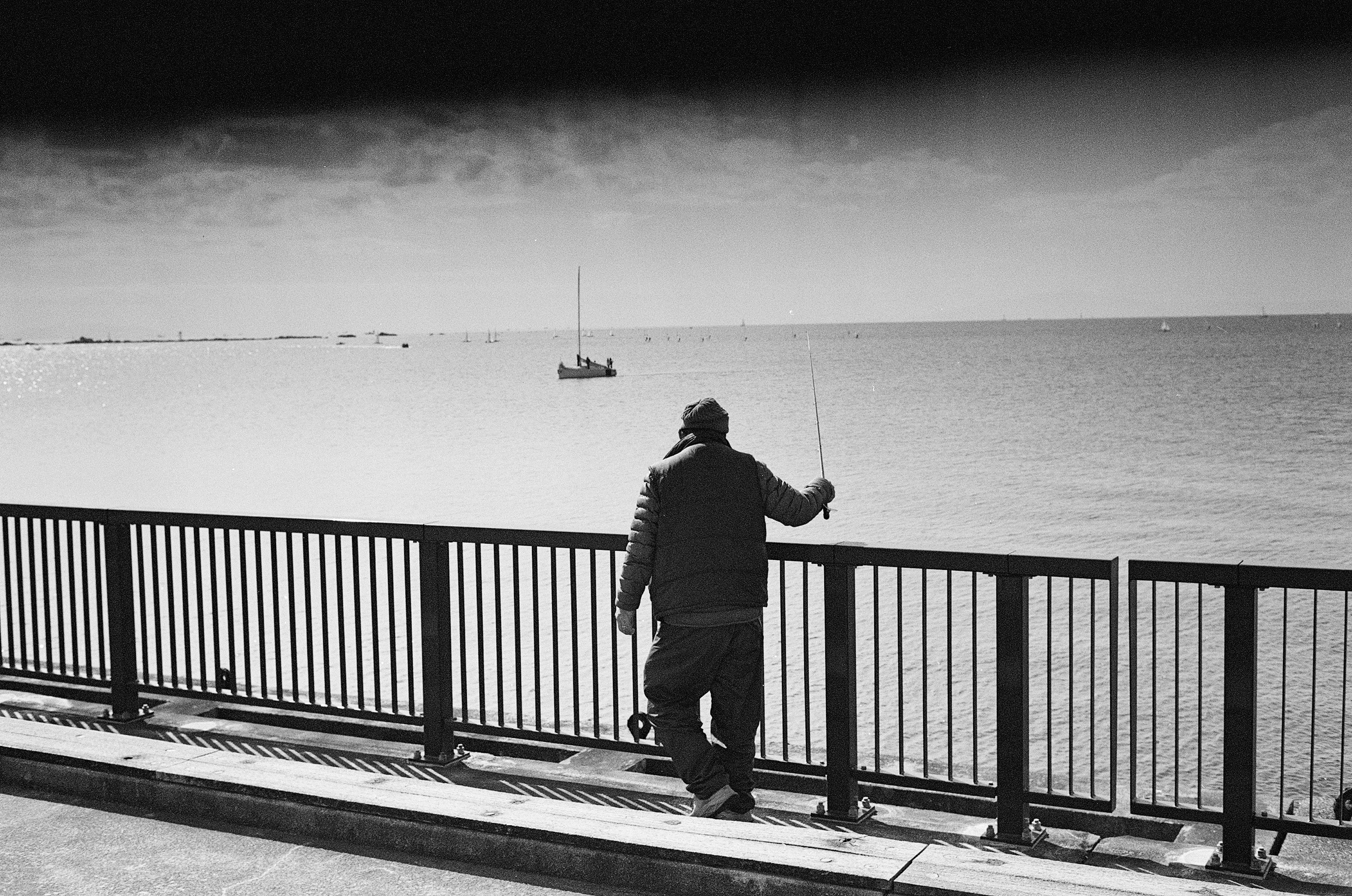 Un hombre sosteniendo una caña de pescar frente al mar en una escena en blanco y negro