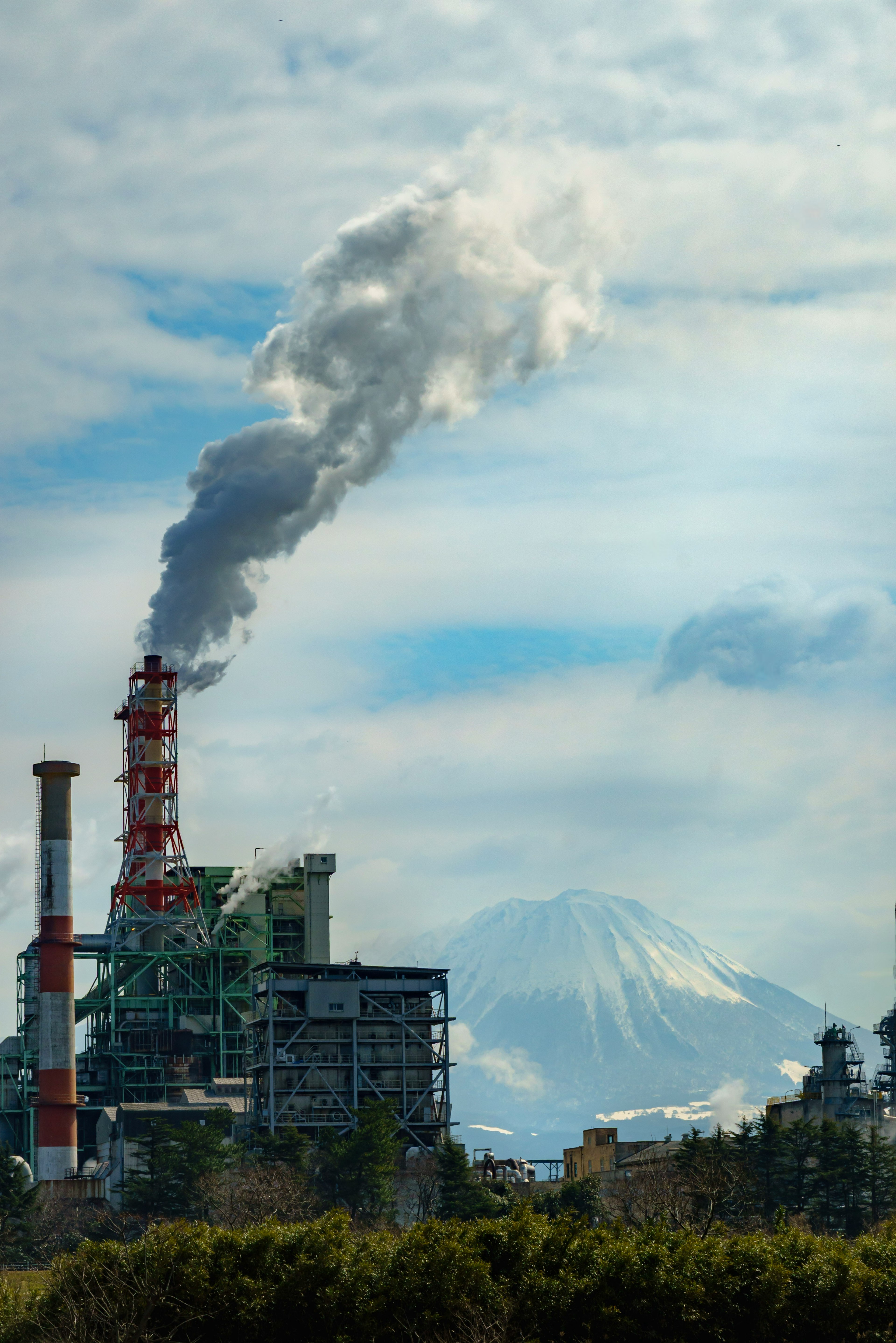 Fábrica emitiendo humo con montaña en el fondo