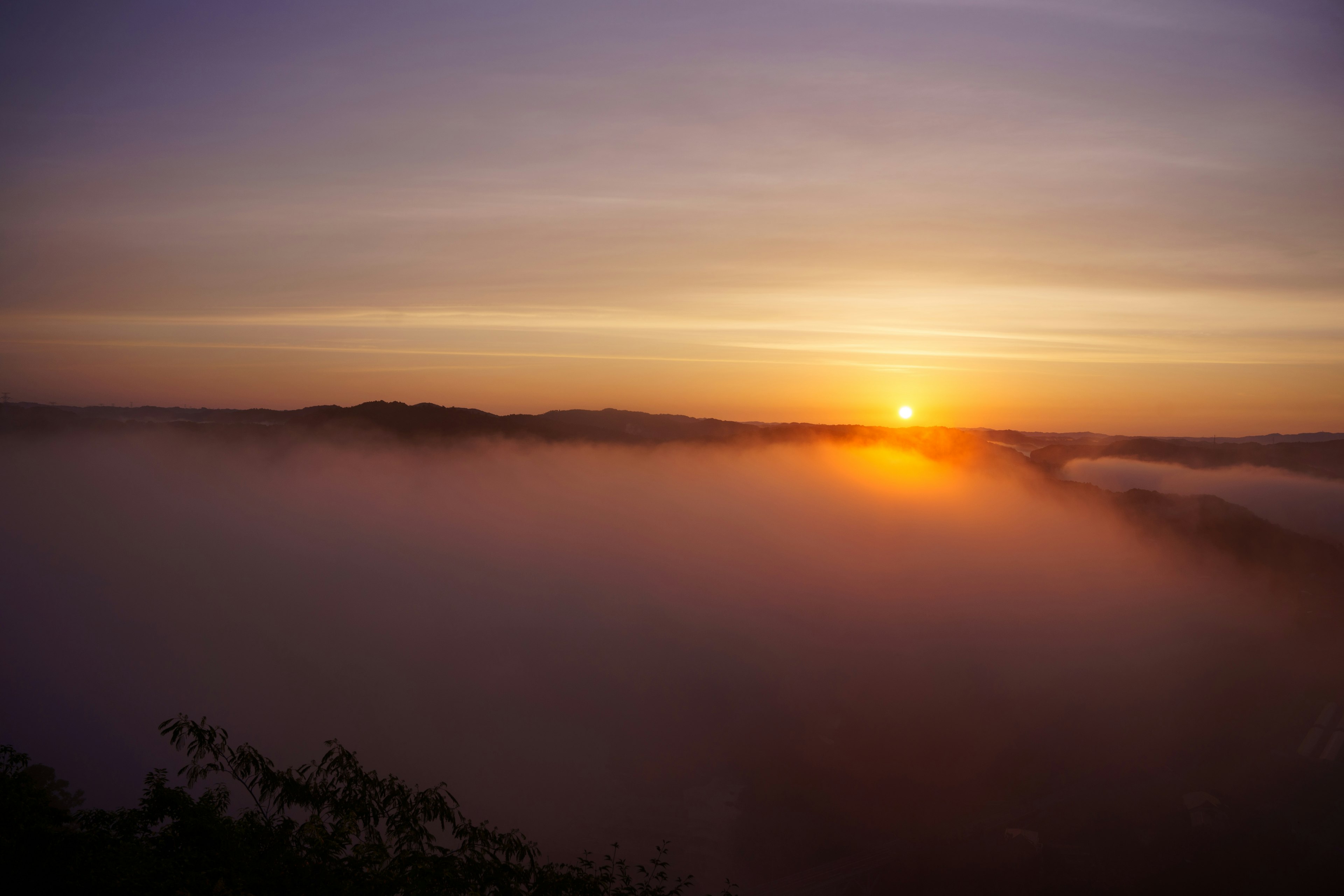 霧に包まれた山々の向こうに昇る太陽の美しい景色