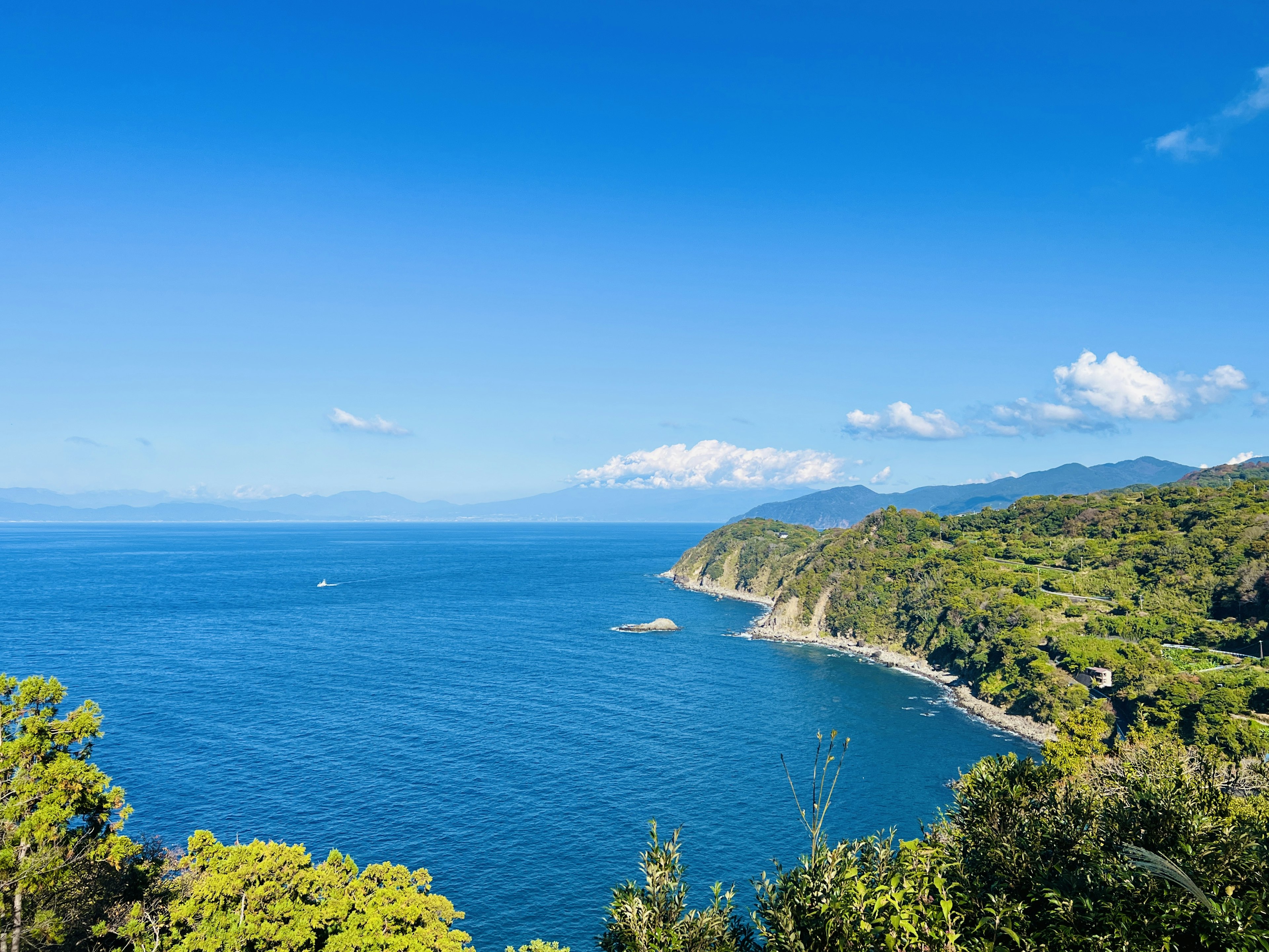 Scenic view of blue ocean and green mountains clear sky and white clouds