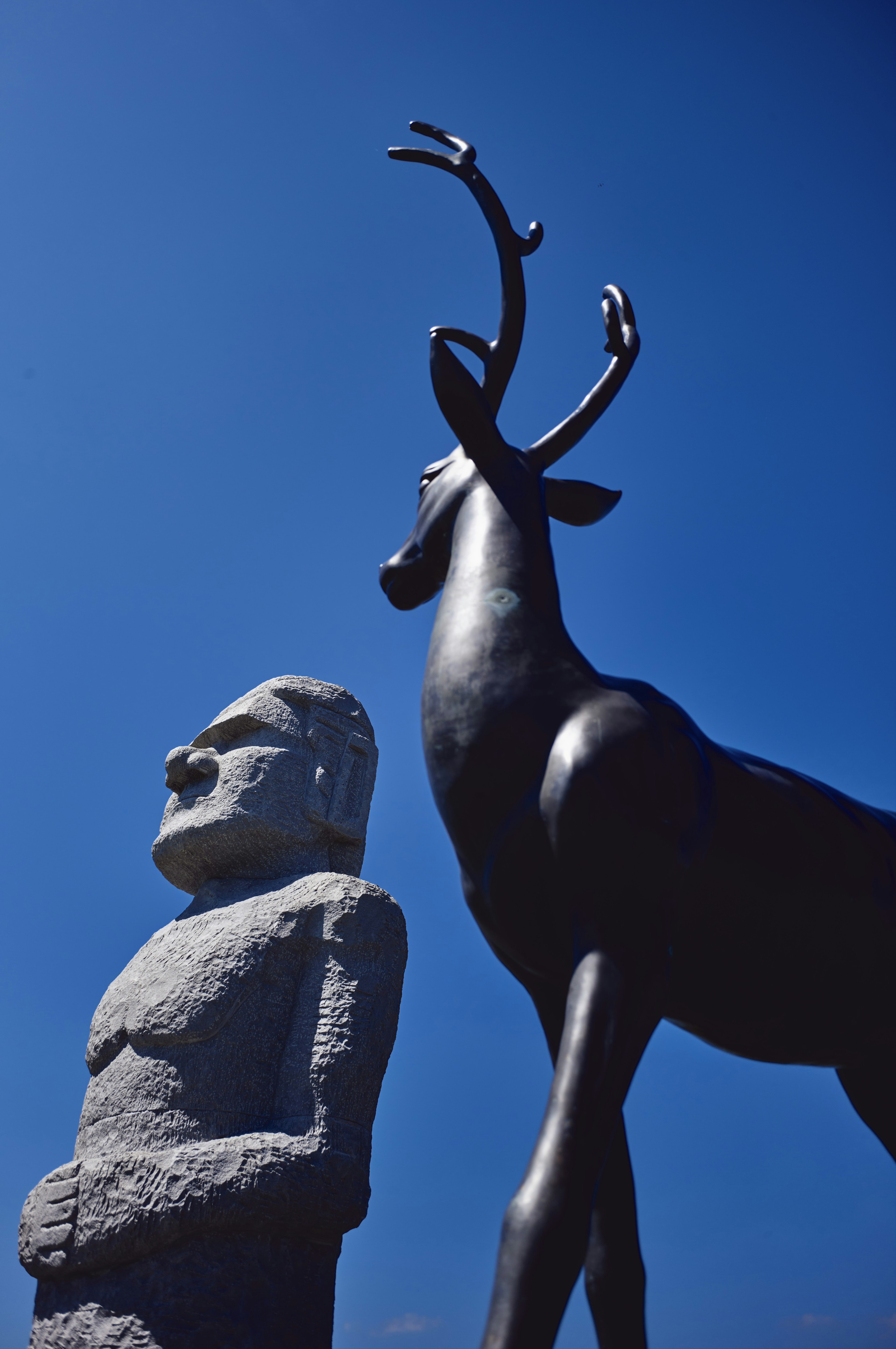 Moai statue and deer sculpture standing under a blue sky