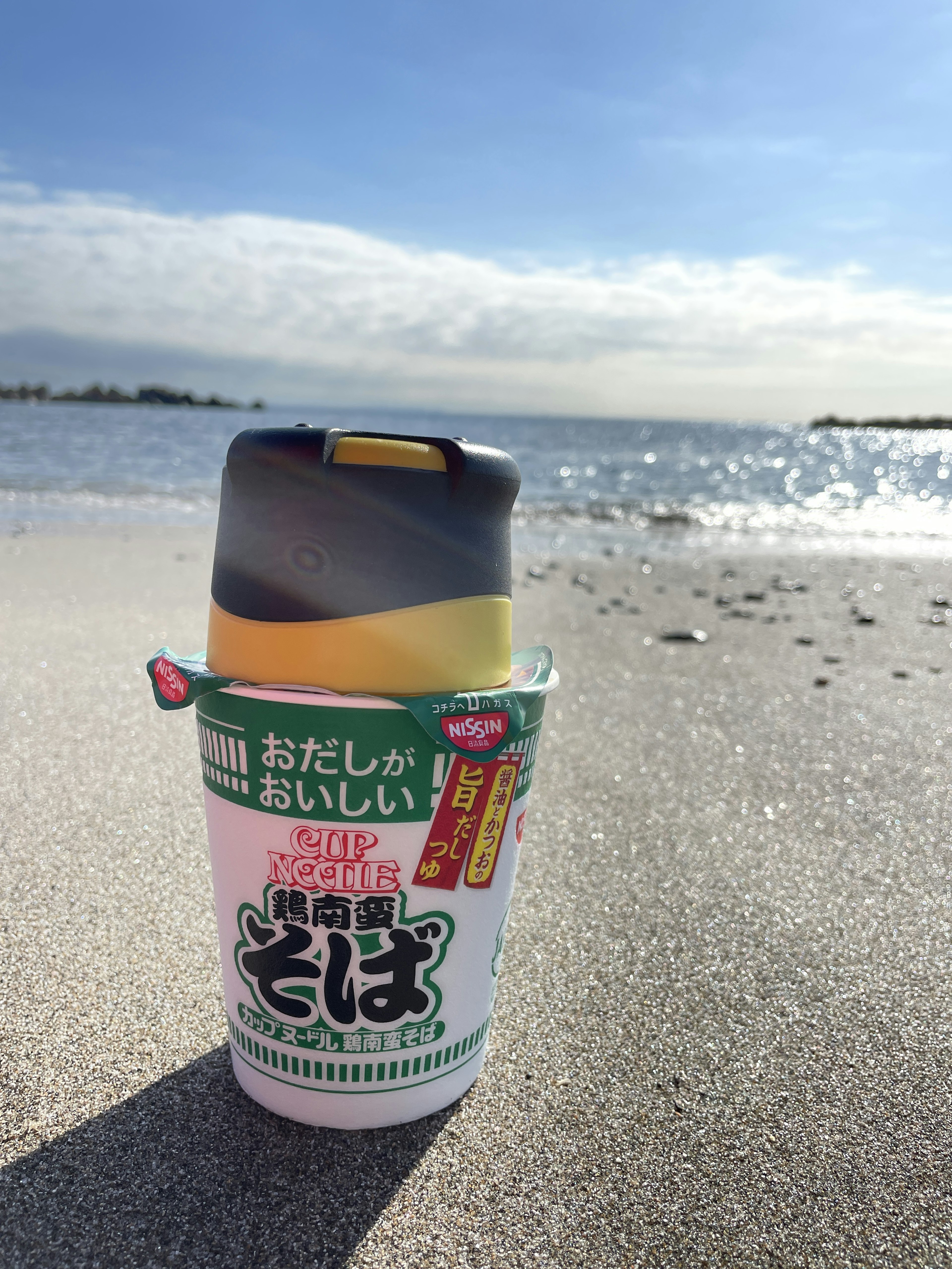 Cup of soba noodles placed on the beach sand