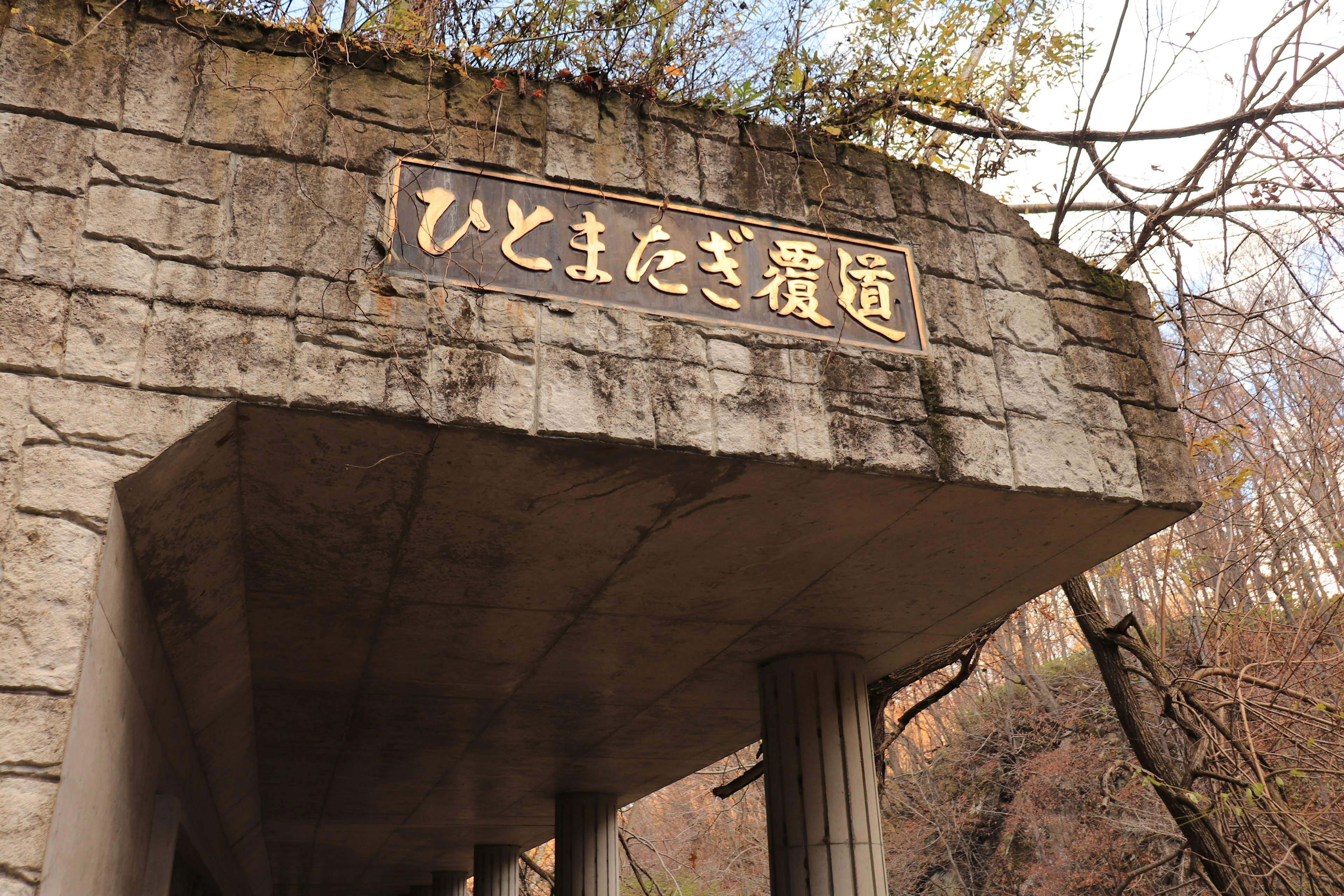 Stone structure marking the entrance to Hitomaza Scenic Path with a sign