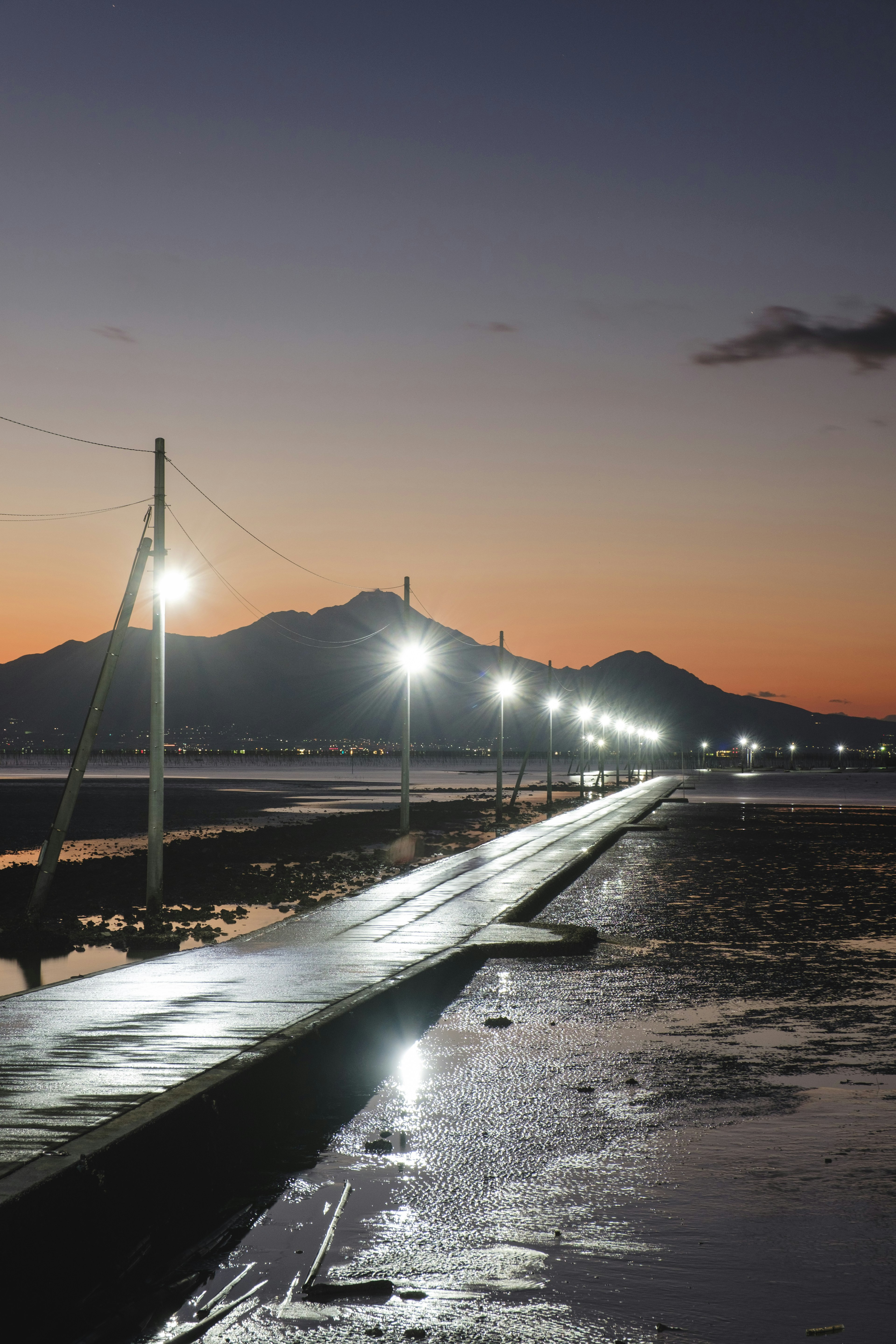 ท่าเทียบเรือริมทะเลที่มีแสงไฟในยามเย็นและภูเขาอยู่เบื้องหลัง