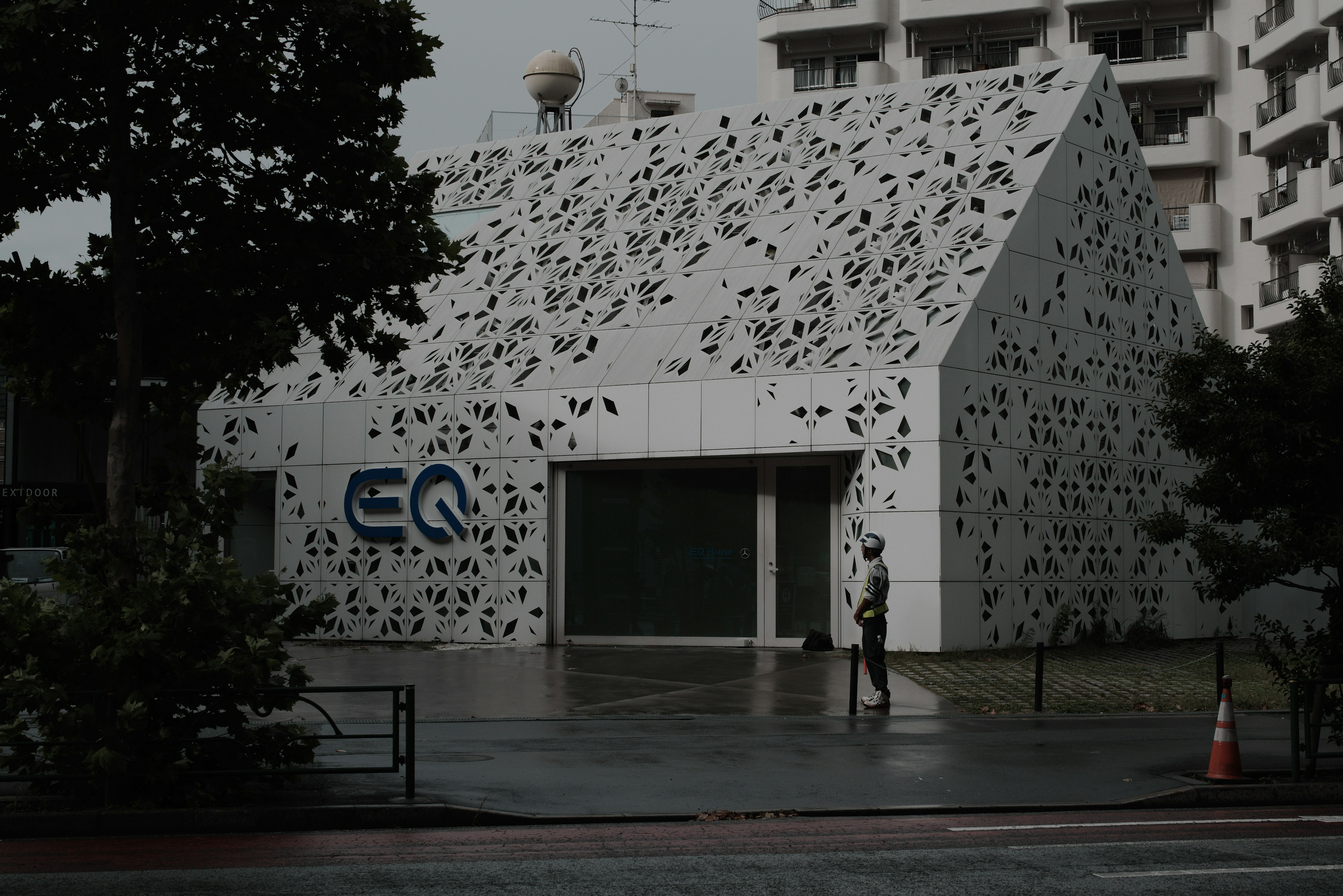 Edificio moderno bianco con logo EQ che presenta un design forato unico persona che cammina sotto la pioggia