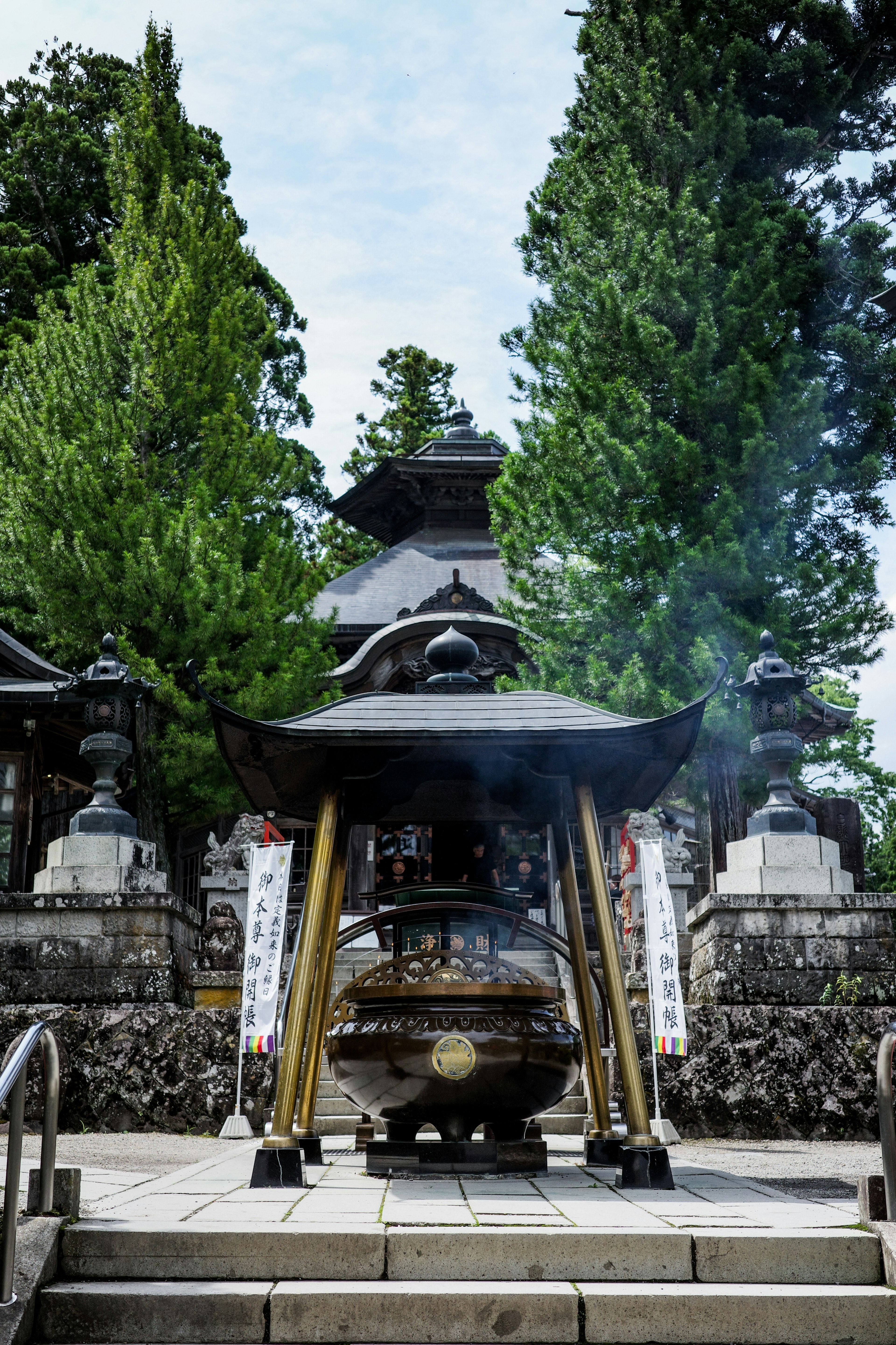 Incense burner in front of a shrine surrounded by lush trees