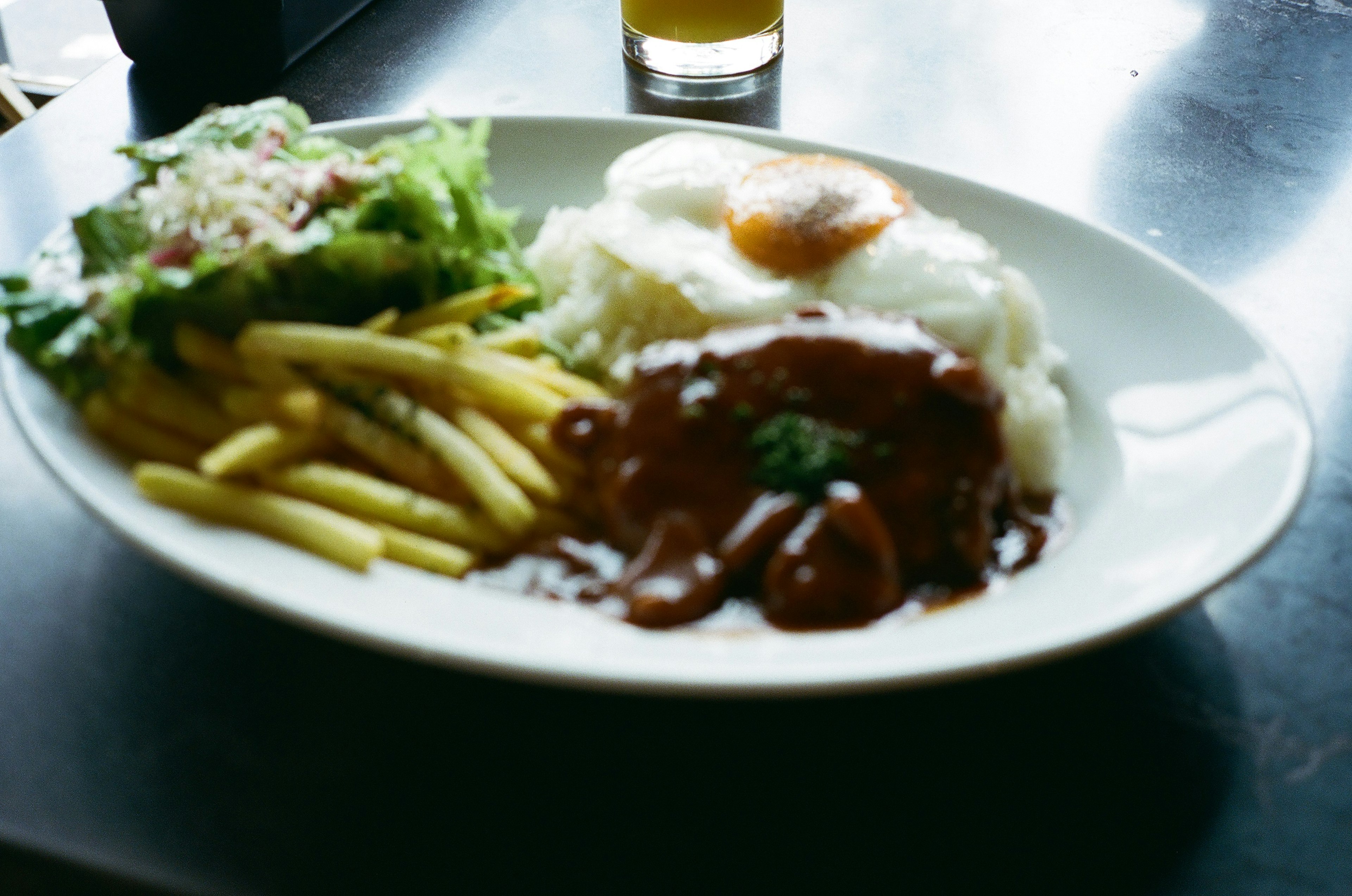 プレートに盛られたご飯と目玉焼き、グレービーソースのかかった肉、フライドポテトとサラダ