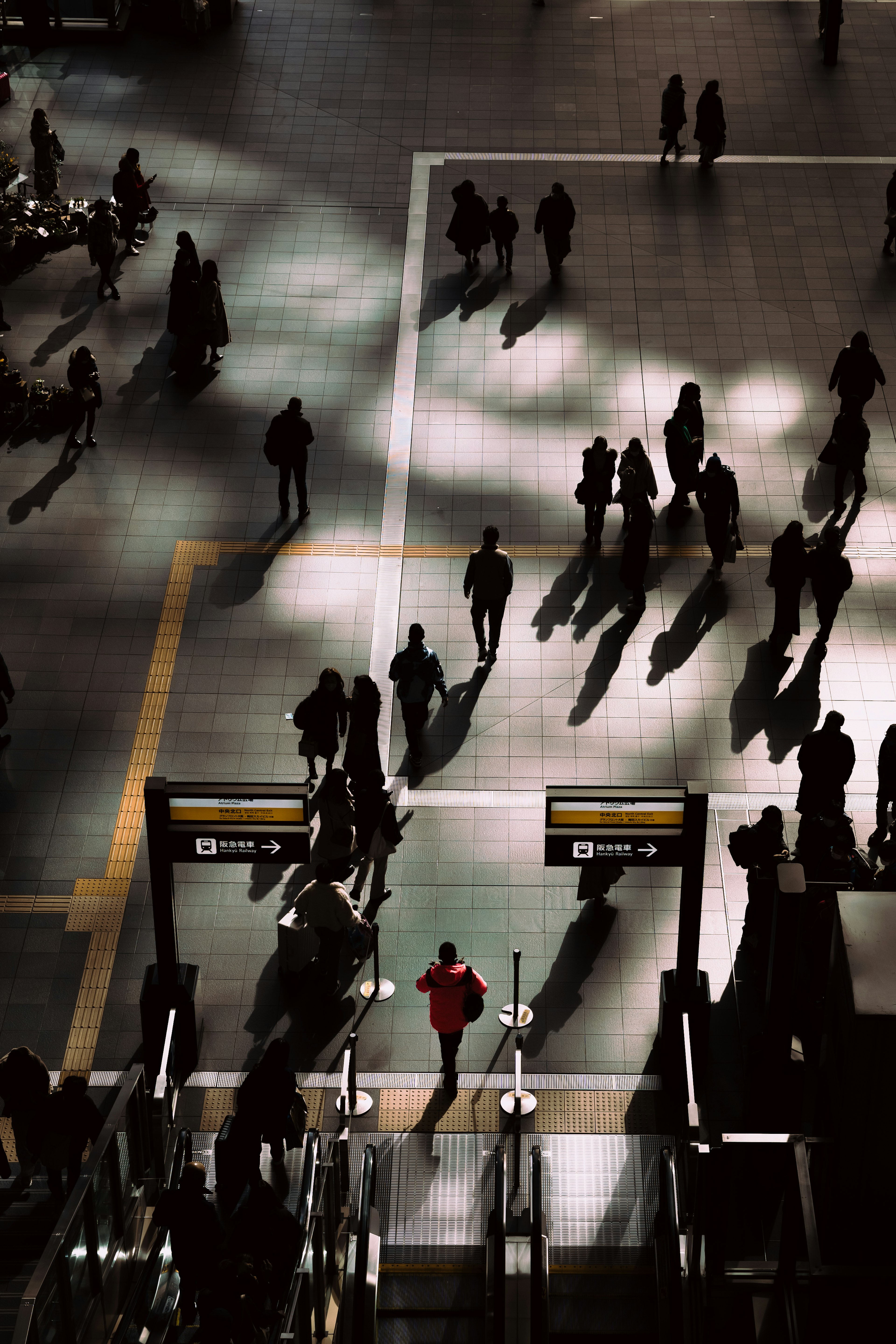 Una escena de estación bulliciosa con sombras de personas Una persona con un atuendo rojo caminando