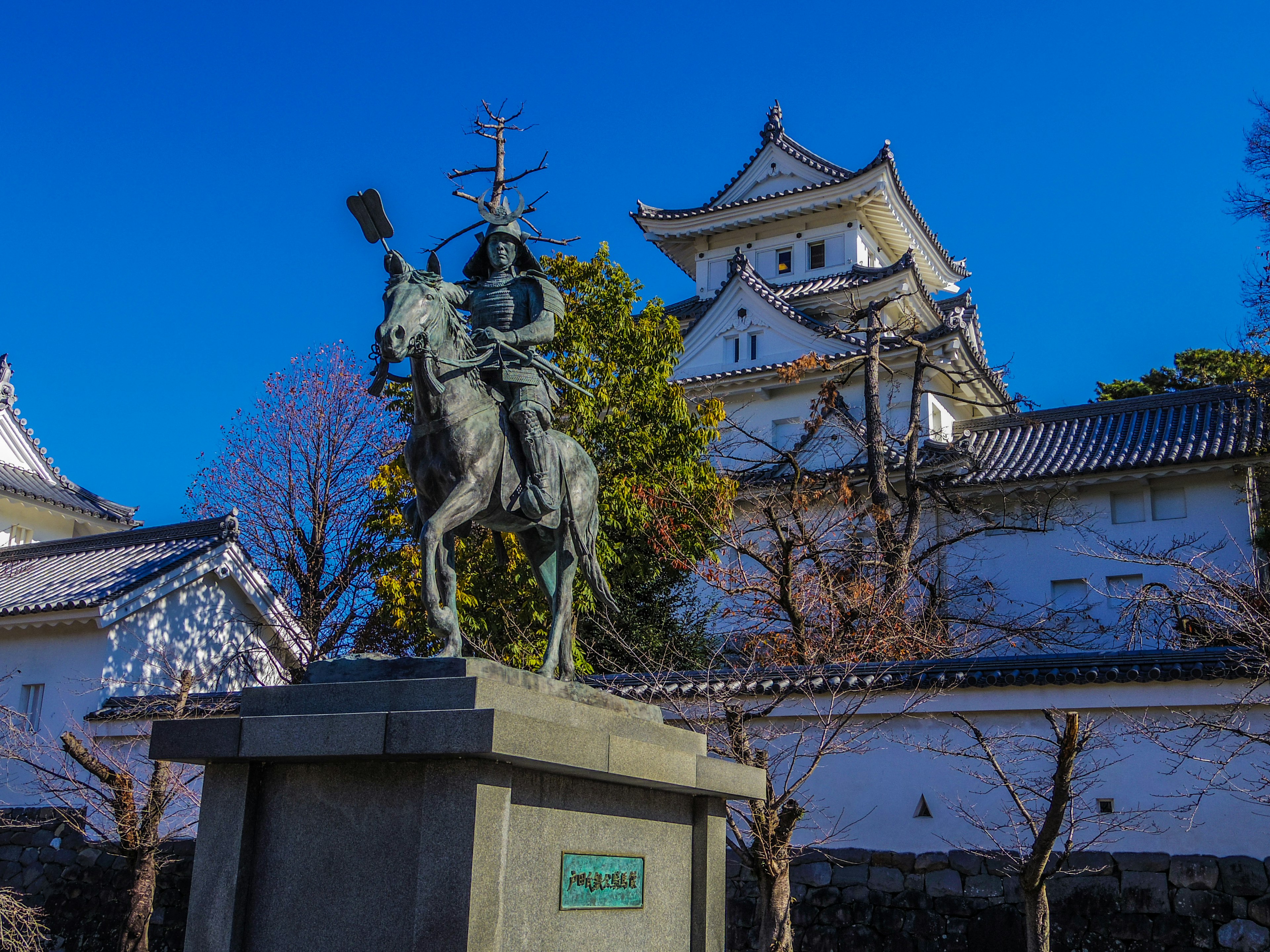 Bronze statue of a mounted samurai with cherry blossoms and a castle in the background