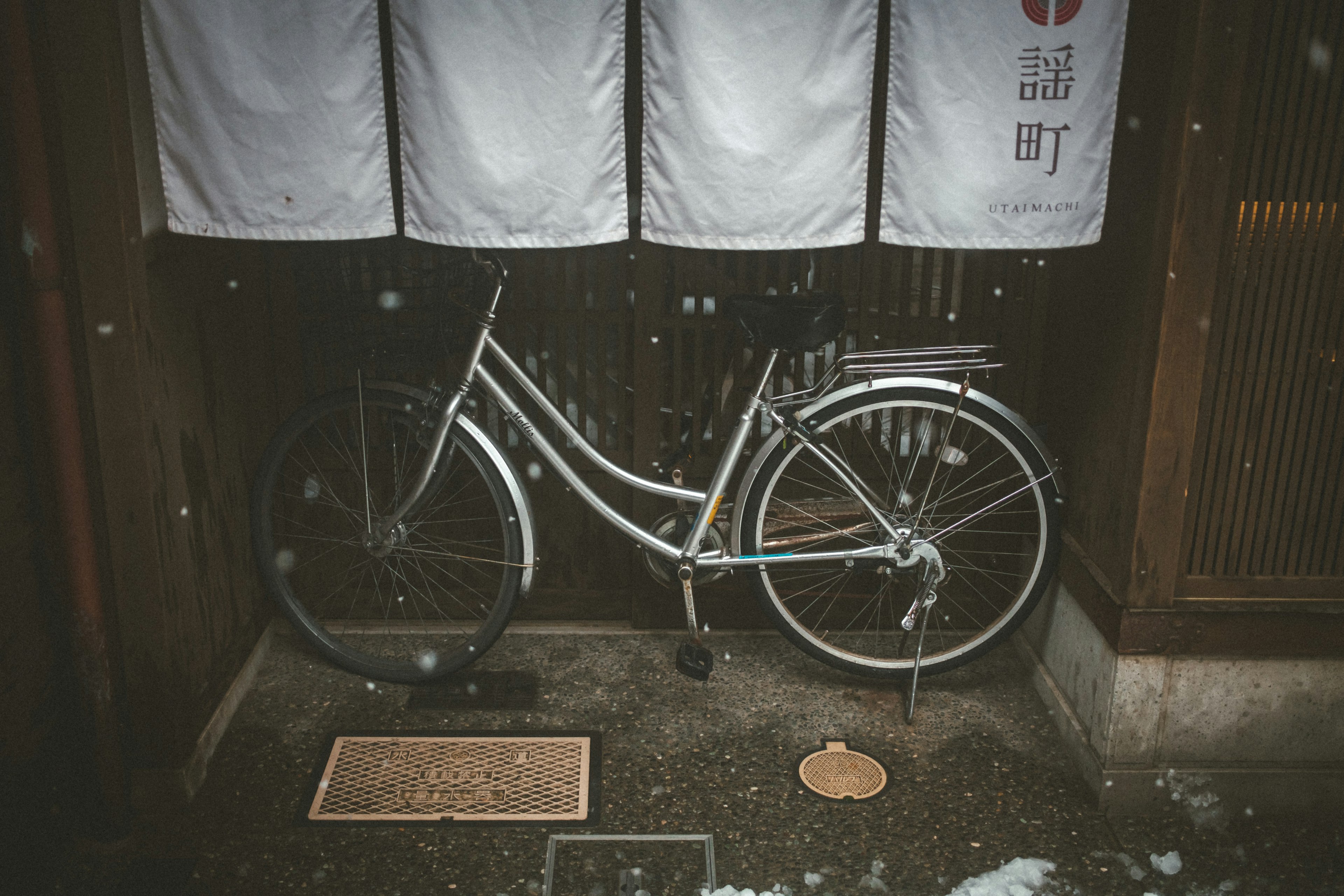 Ein weißes Fahrrad im Schnee neben einem traditionellen japanischen Eingang mit Noren-Vorhängen